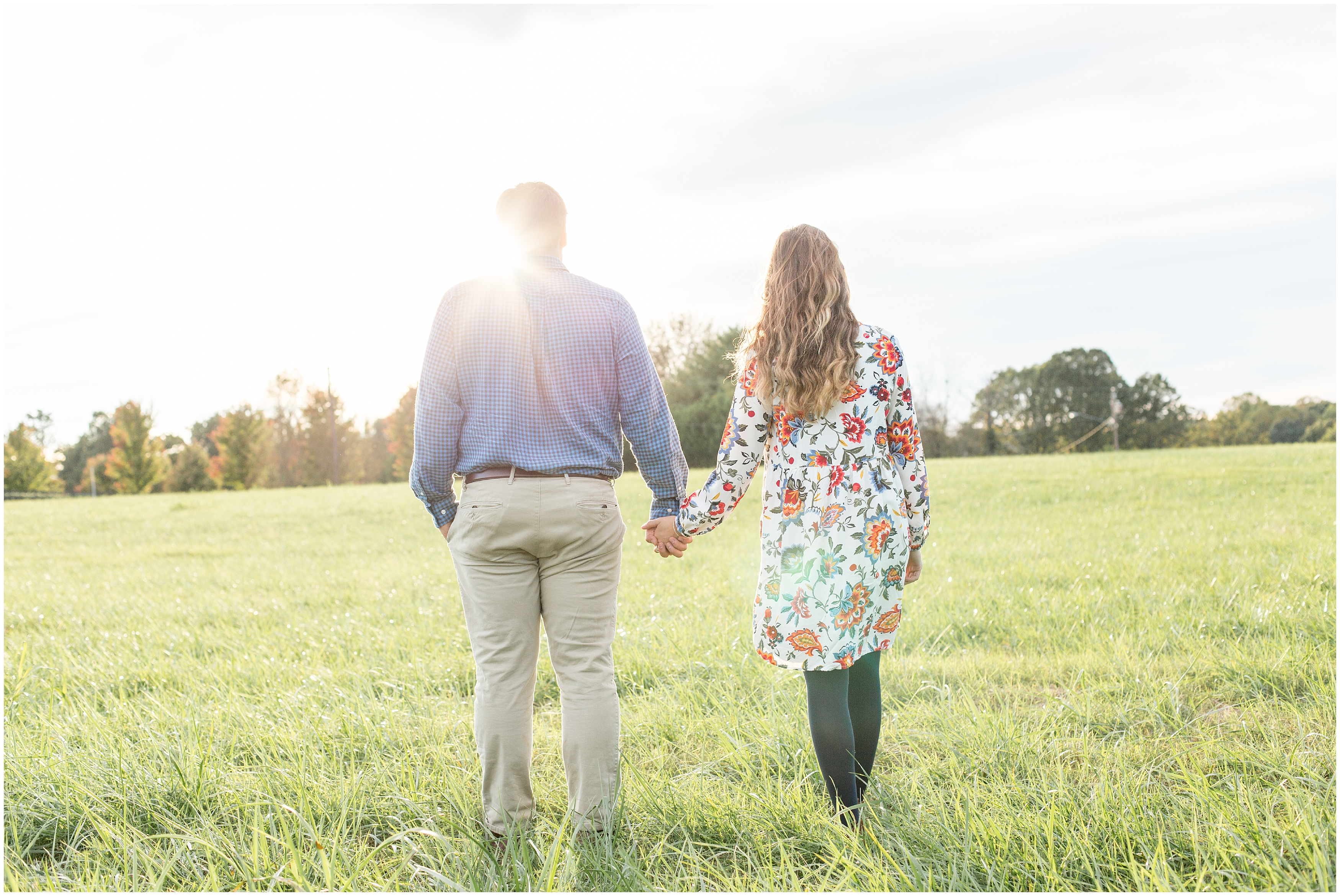 couple holds hands walking in grass during engagement session