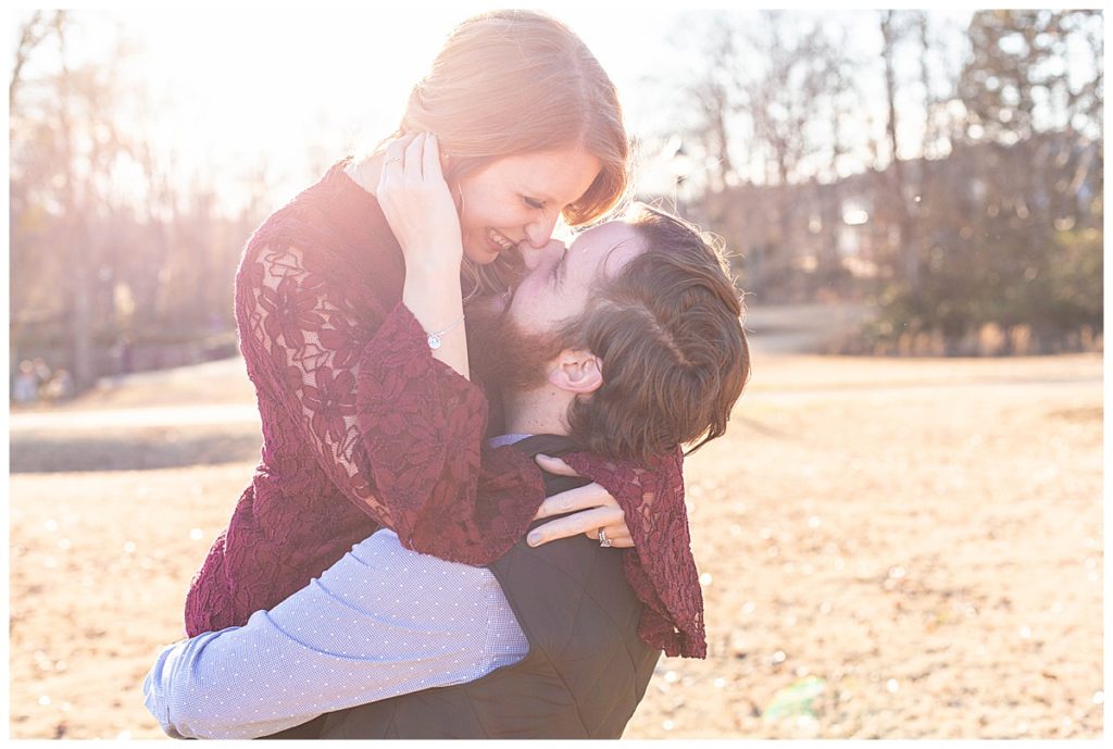 Engaged couple kiss with the sunlight behind them in Greenville SC