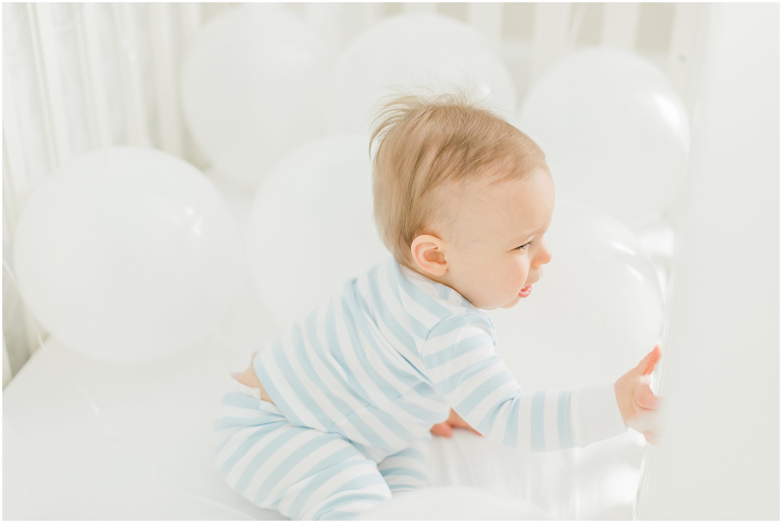 baby plays with white balloons in crib