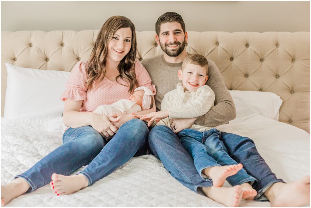 parents sit on bed with kids during newborn session at home