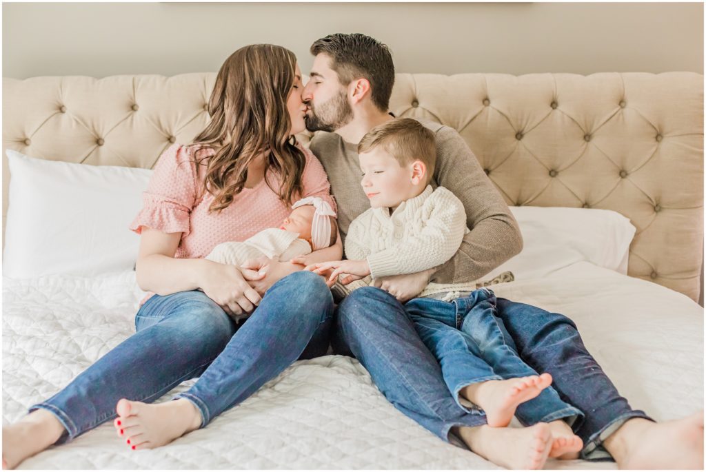 parents kiss while holding two kids during Charlotte newborn session