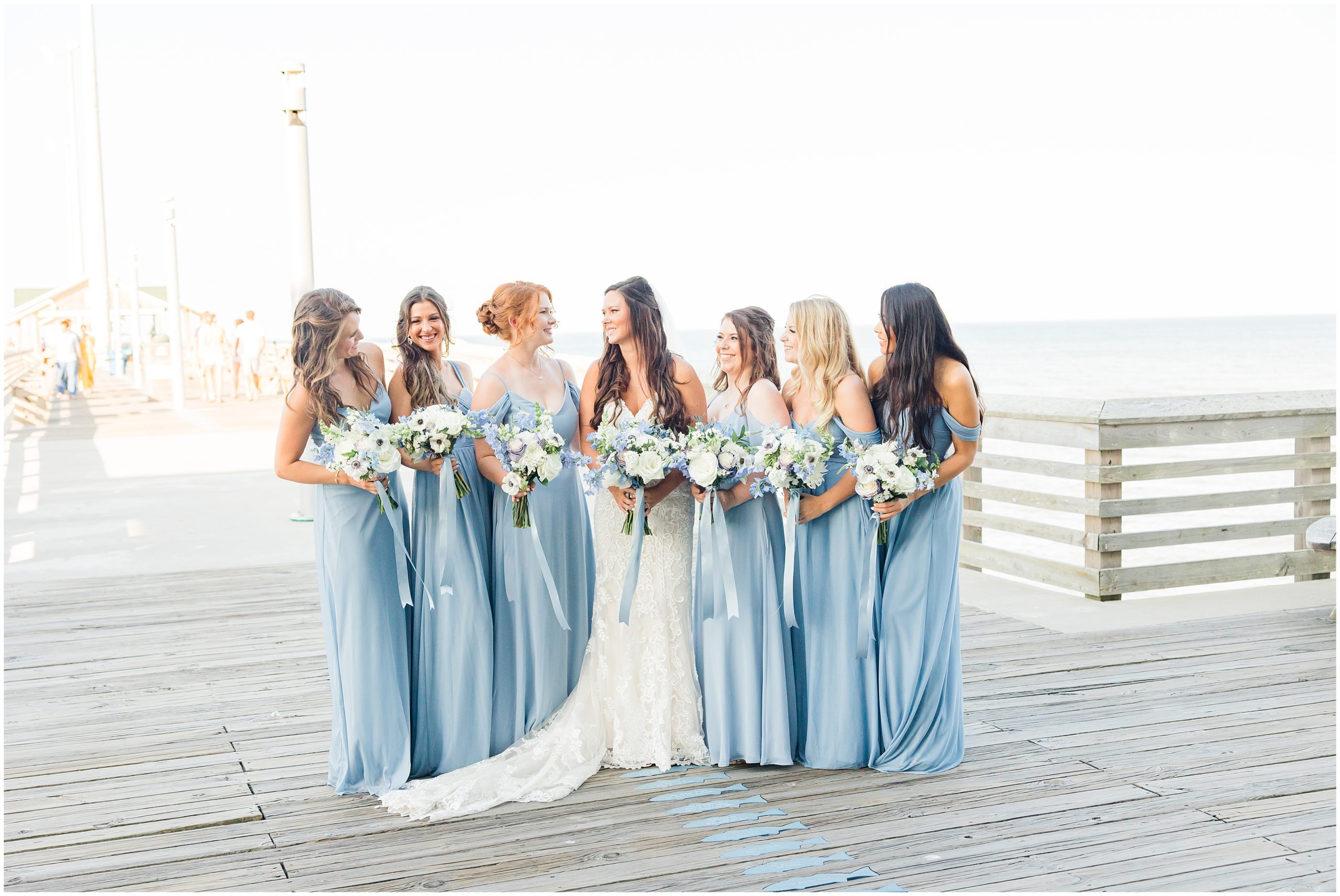 bride and bridesmaids in light blue gowns pose on pier in Outer Banks