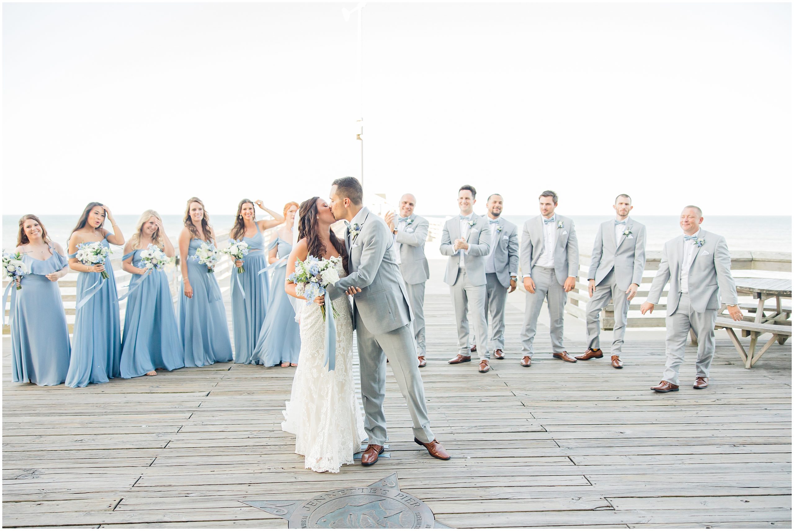 bride and groom kiss on Jennette's Pier with wedding party behind them