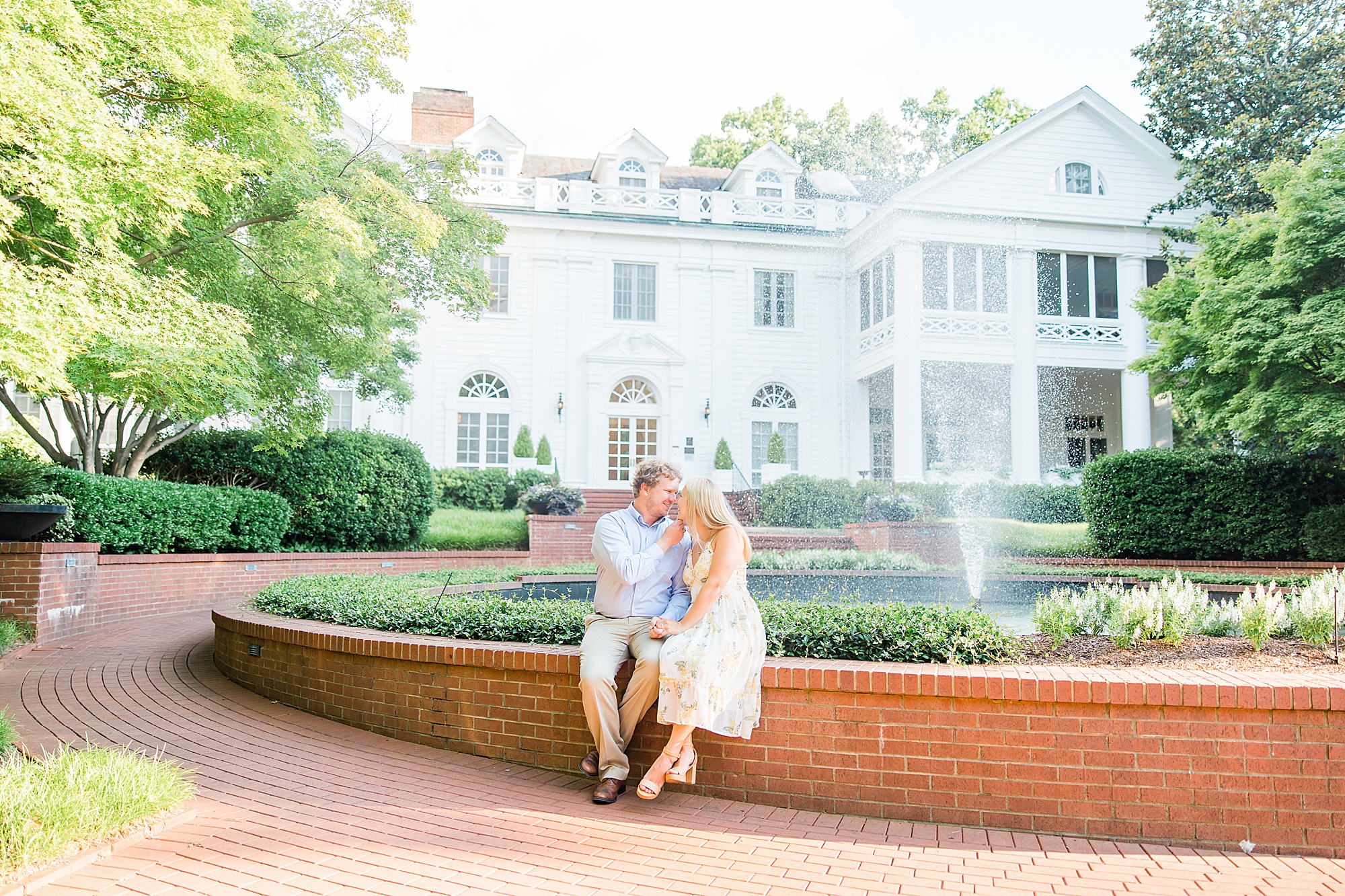 engaged couple sits on brick wall outside the Duke Mansion