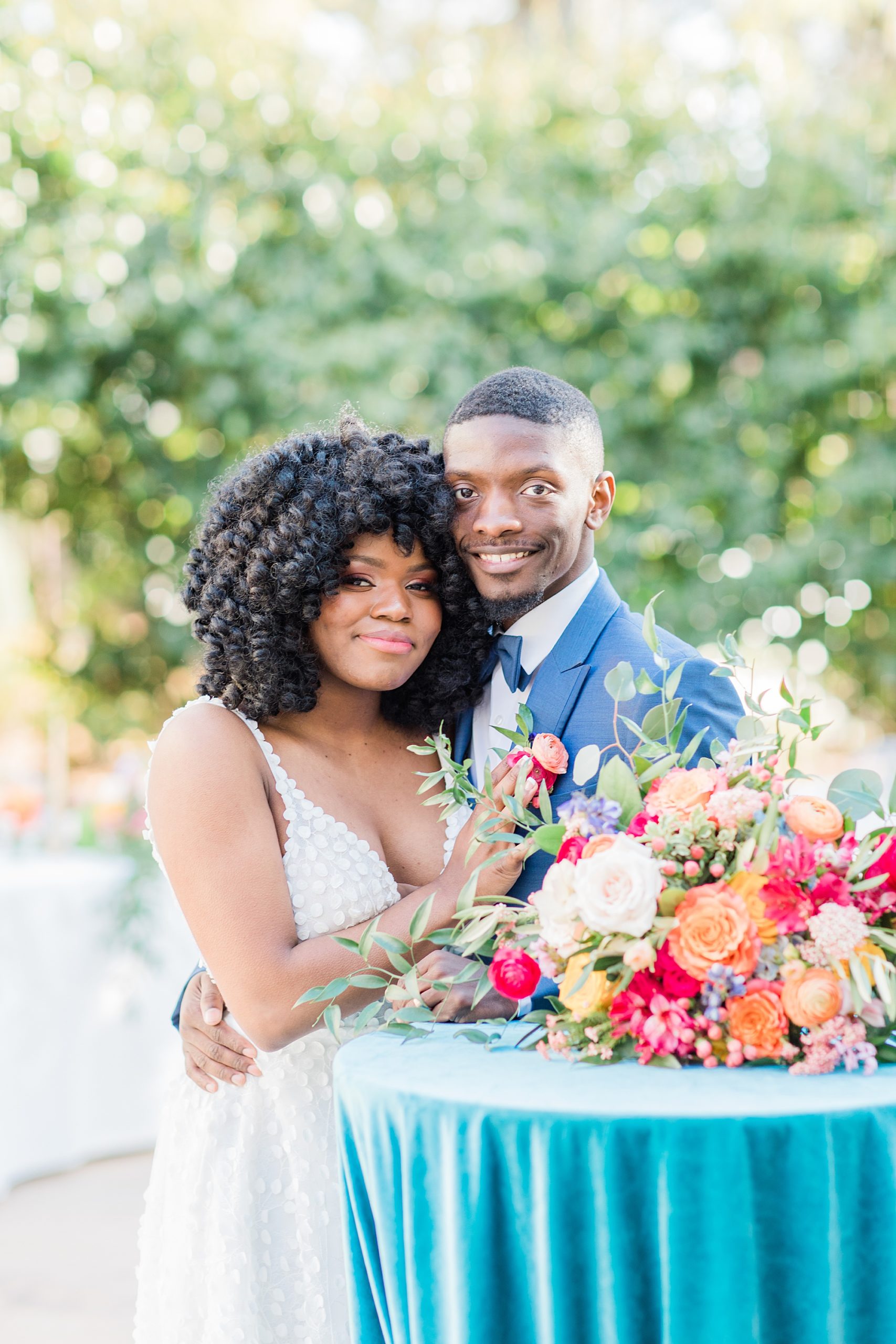 newlyweds hug by table with big colorful floral display