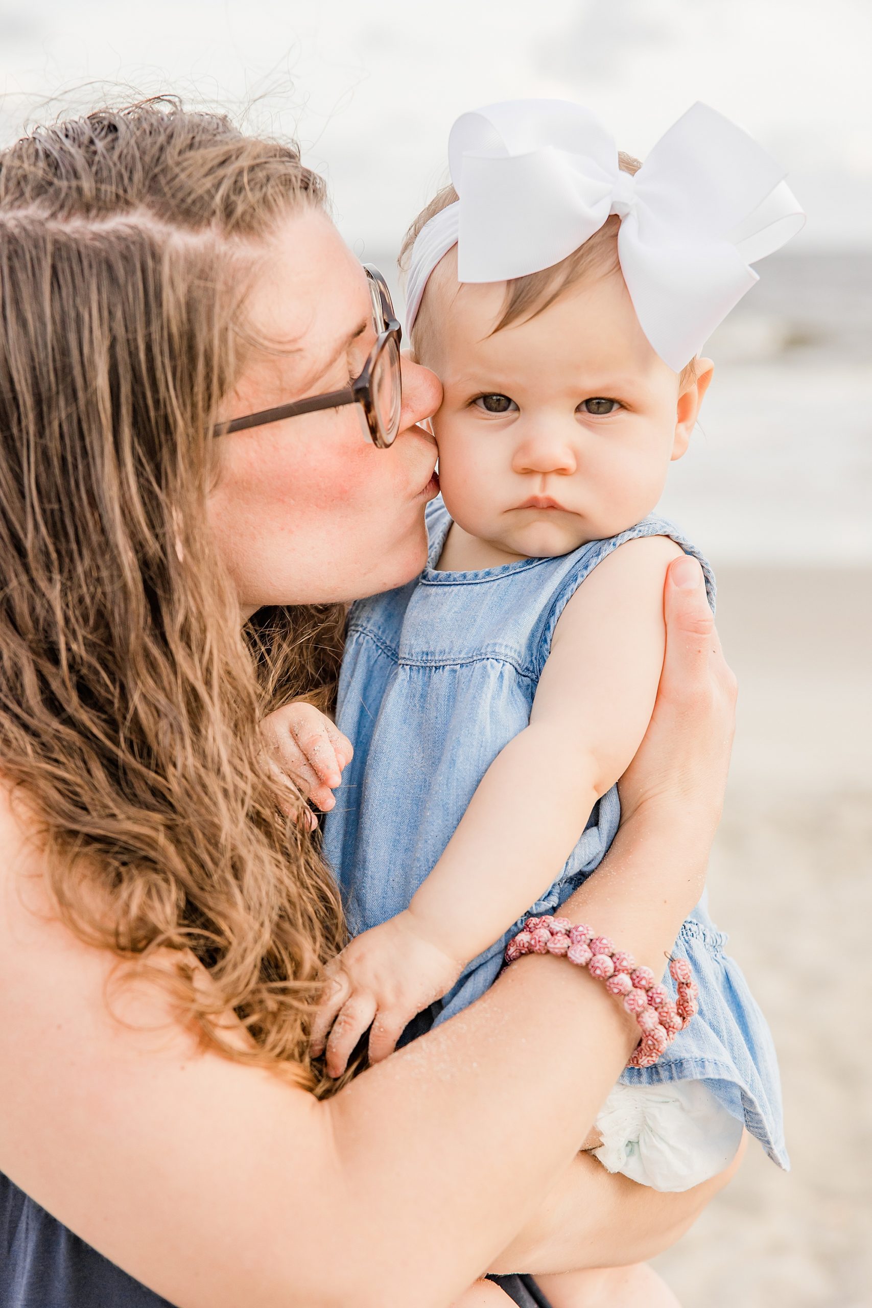 woman kisses toddler pouting with white bow on head