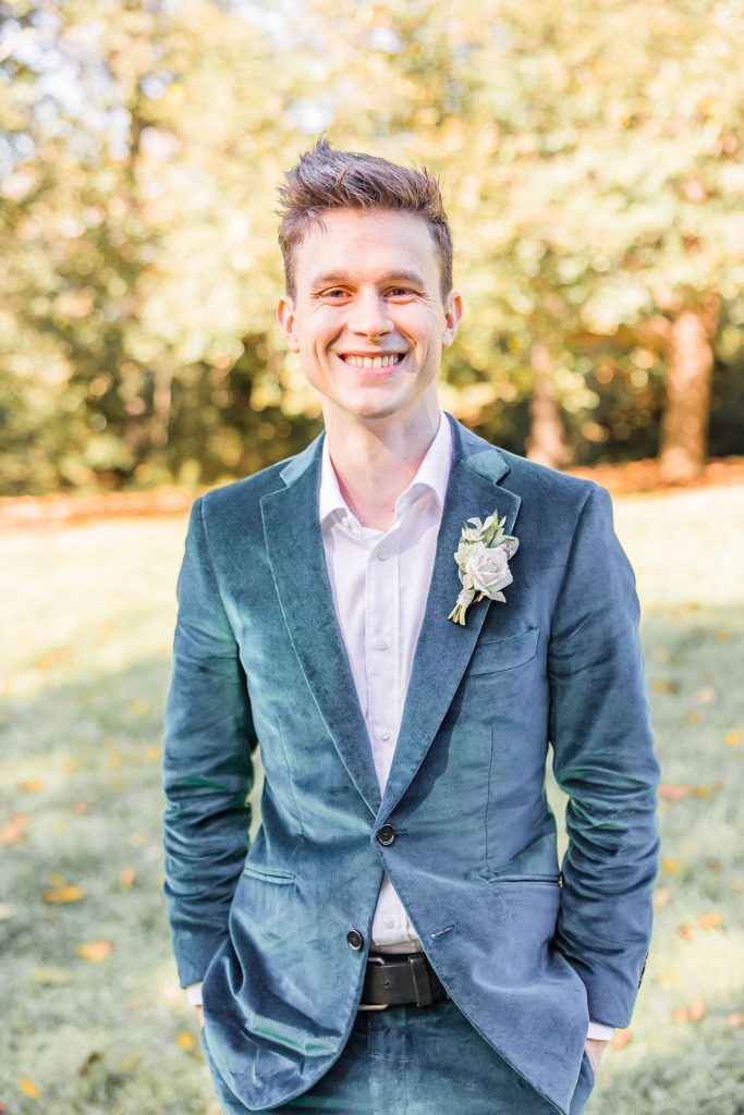 groom smiles in green velvet jacket on fall wedding day 