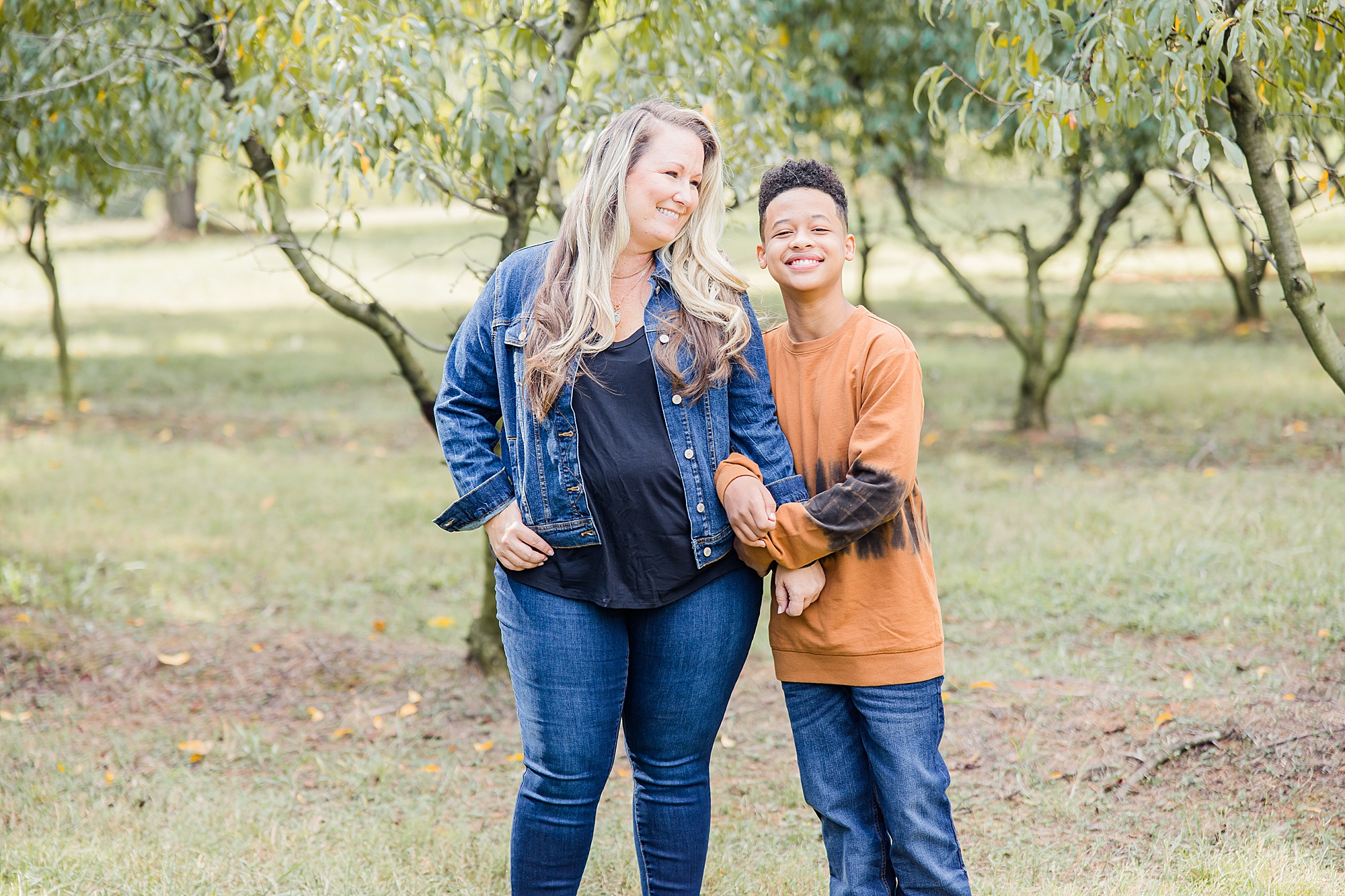 son holds mom's arm standing among trees during fall Charlotte family portraits