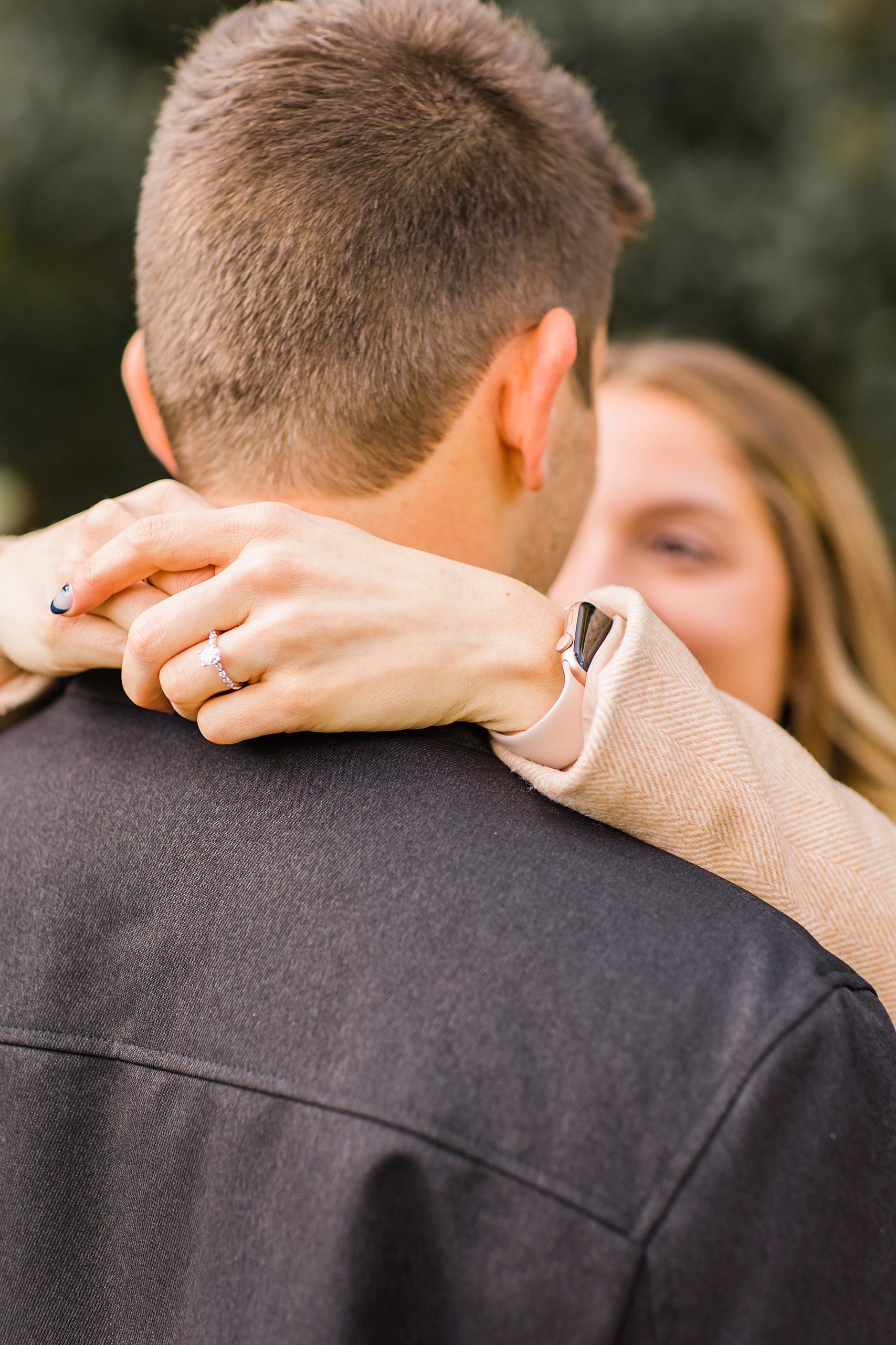 woman hugs fiancee showing off ring behind his head