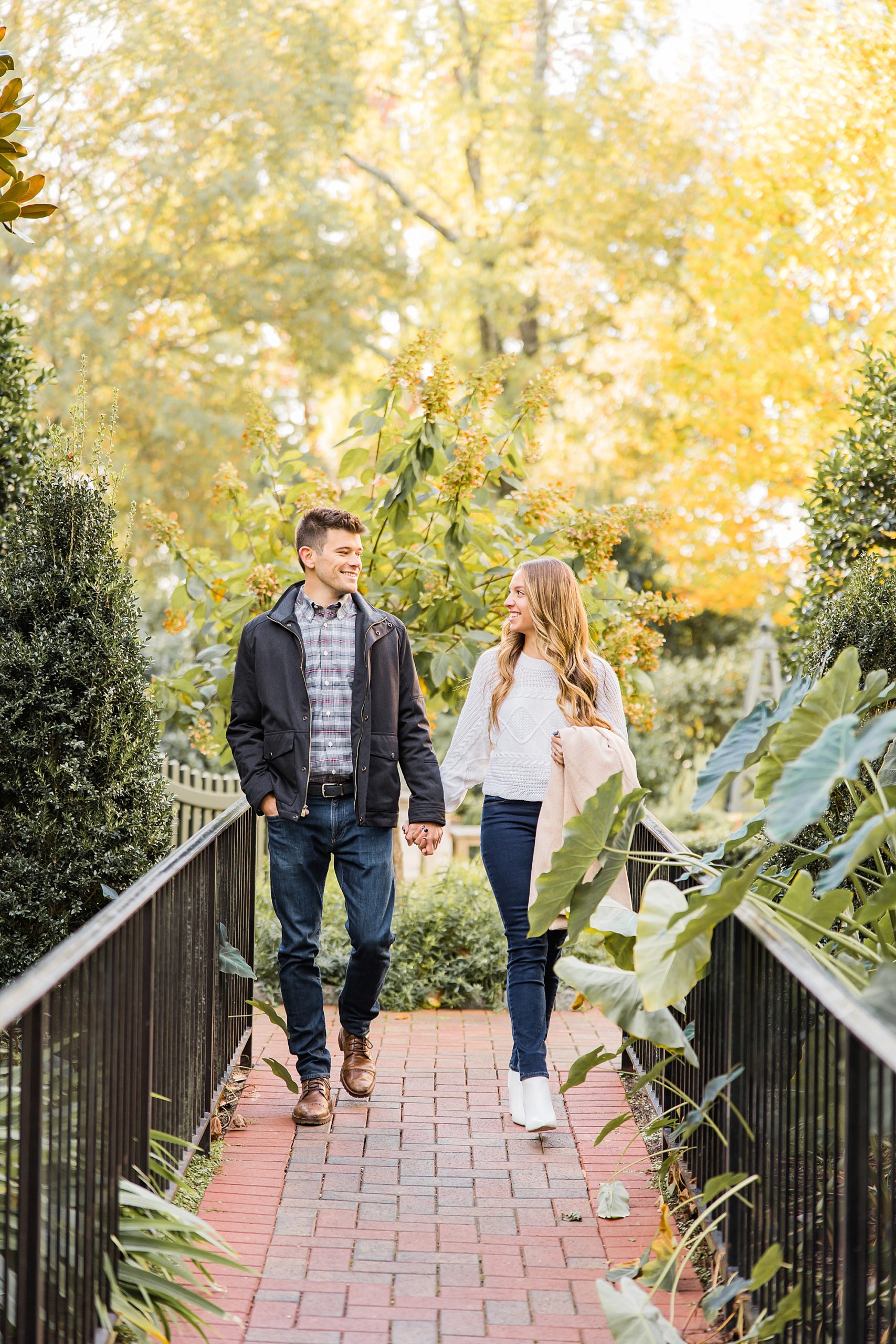 couple holds hands walking through gardens at Duke Mansion