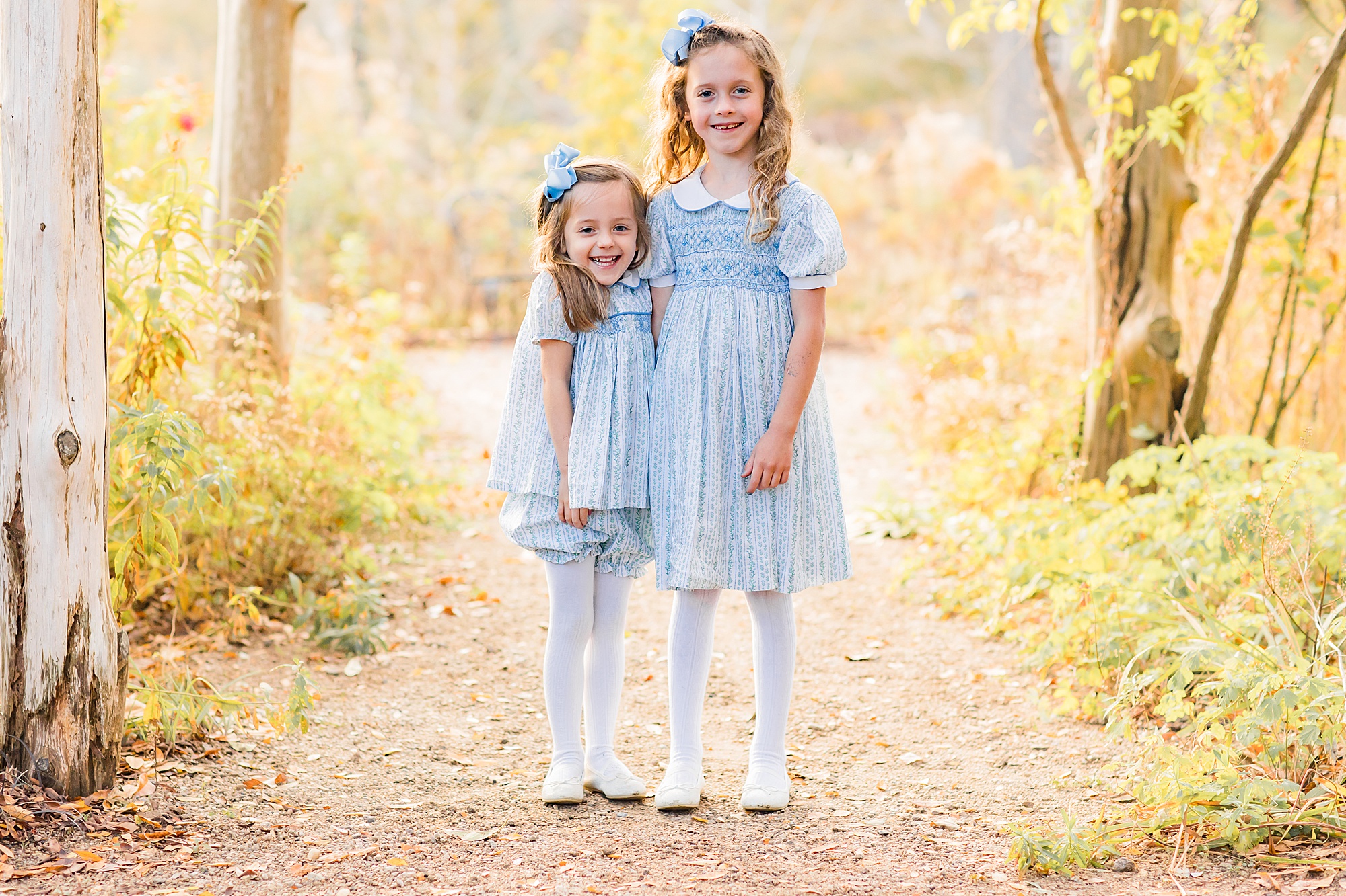sisters in matching blue dresses stand together during fall family photos
