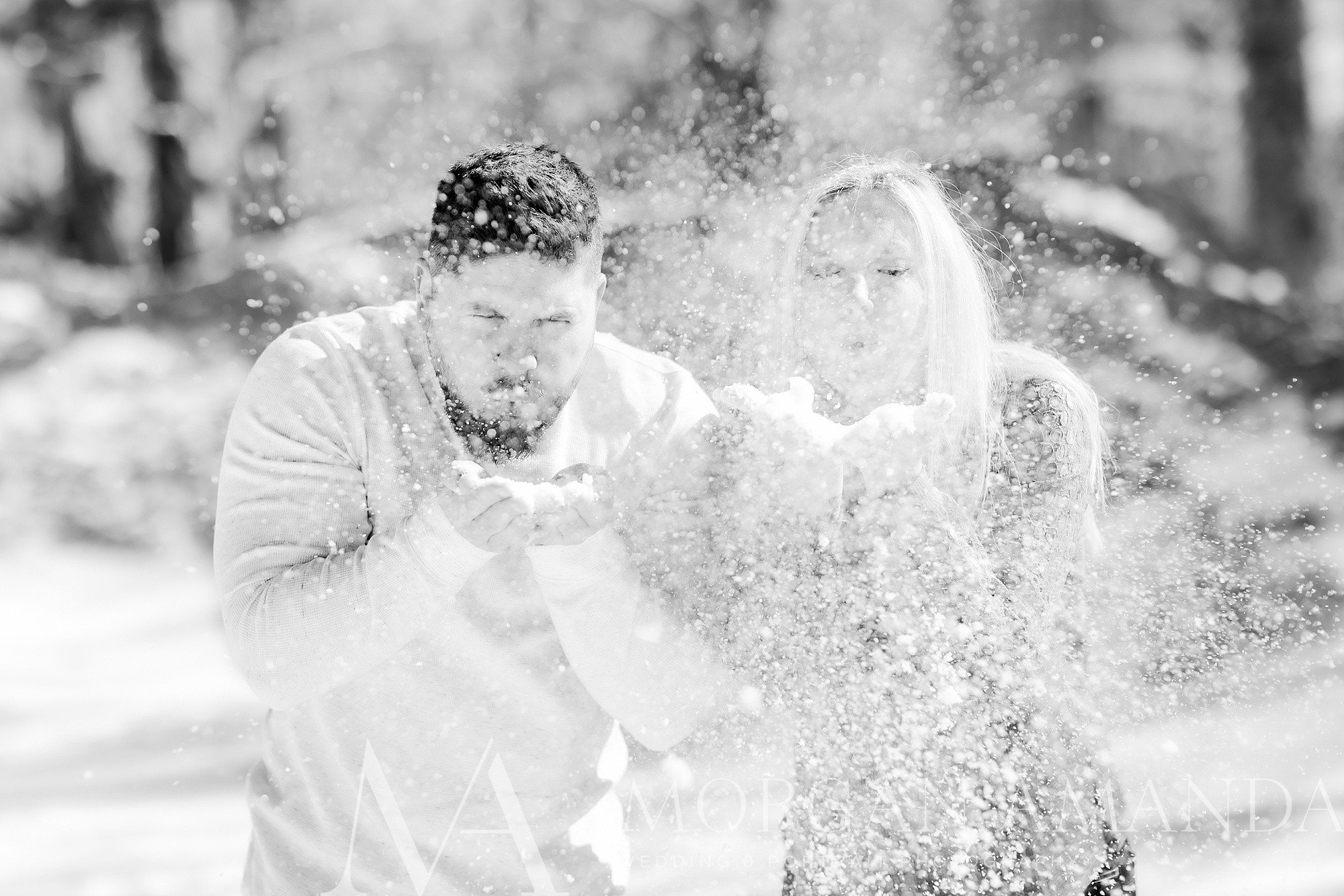 engaged couple blows snow during photos at Beech Mountain