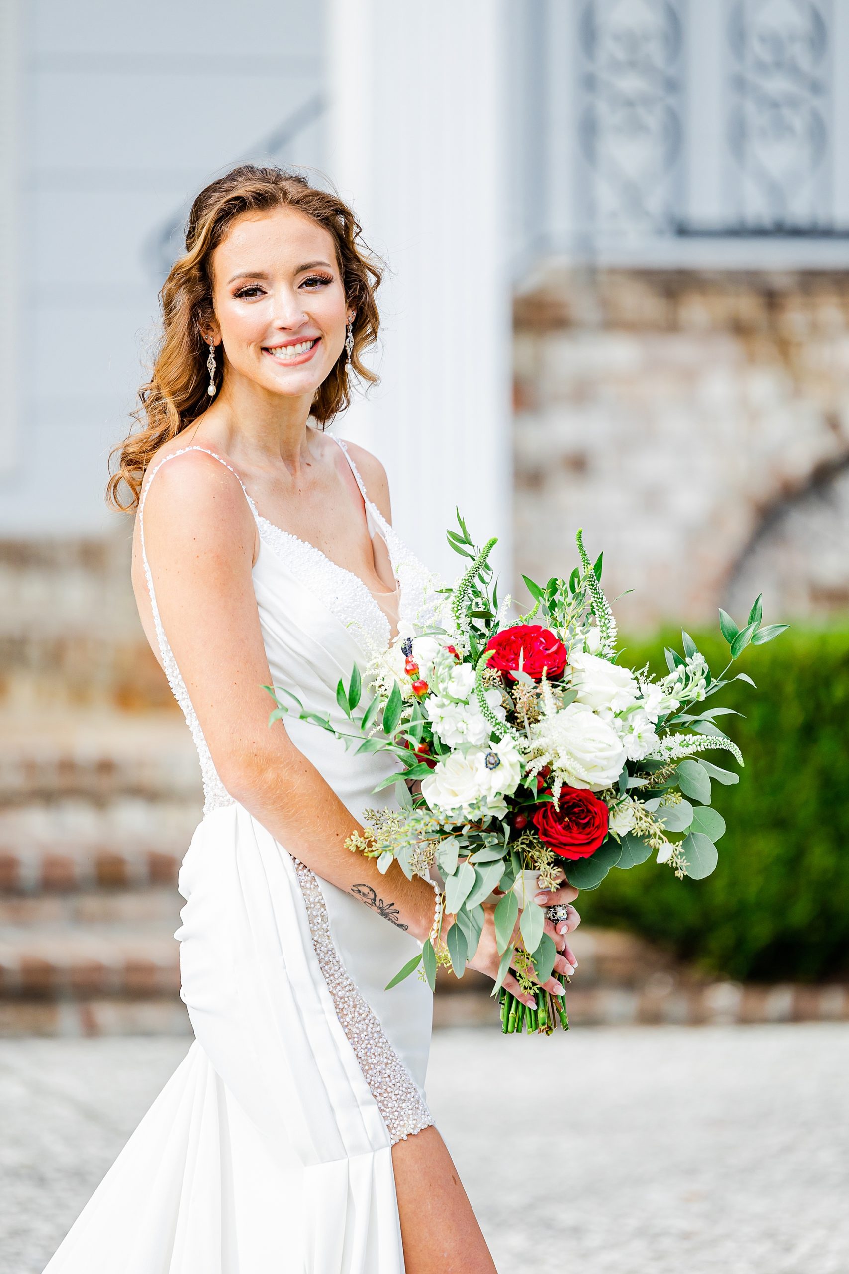 bride stands holding bouquet of red and white roses outside the Island House