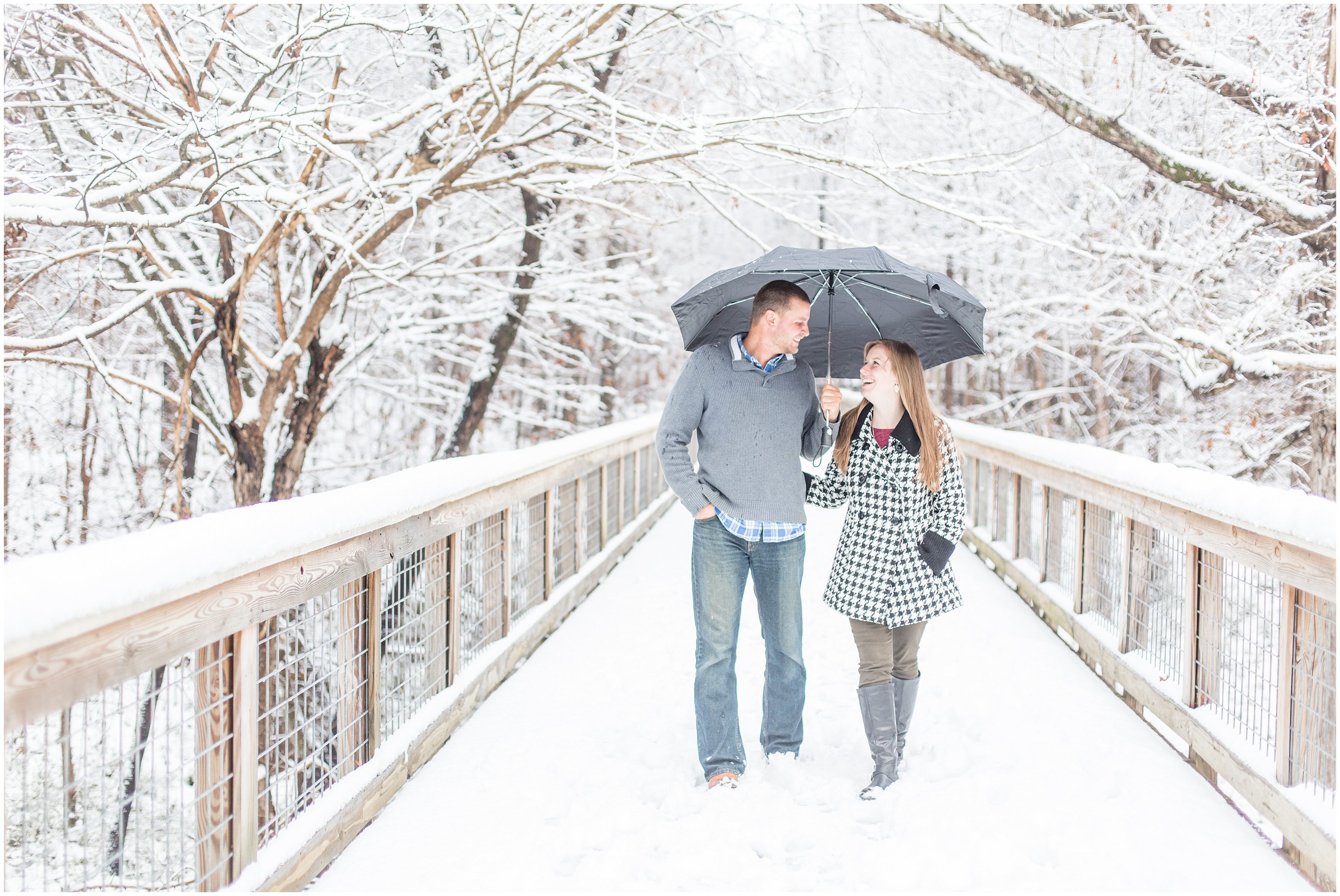 couple walk across a snow covered bridge with an umbrella in GA