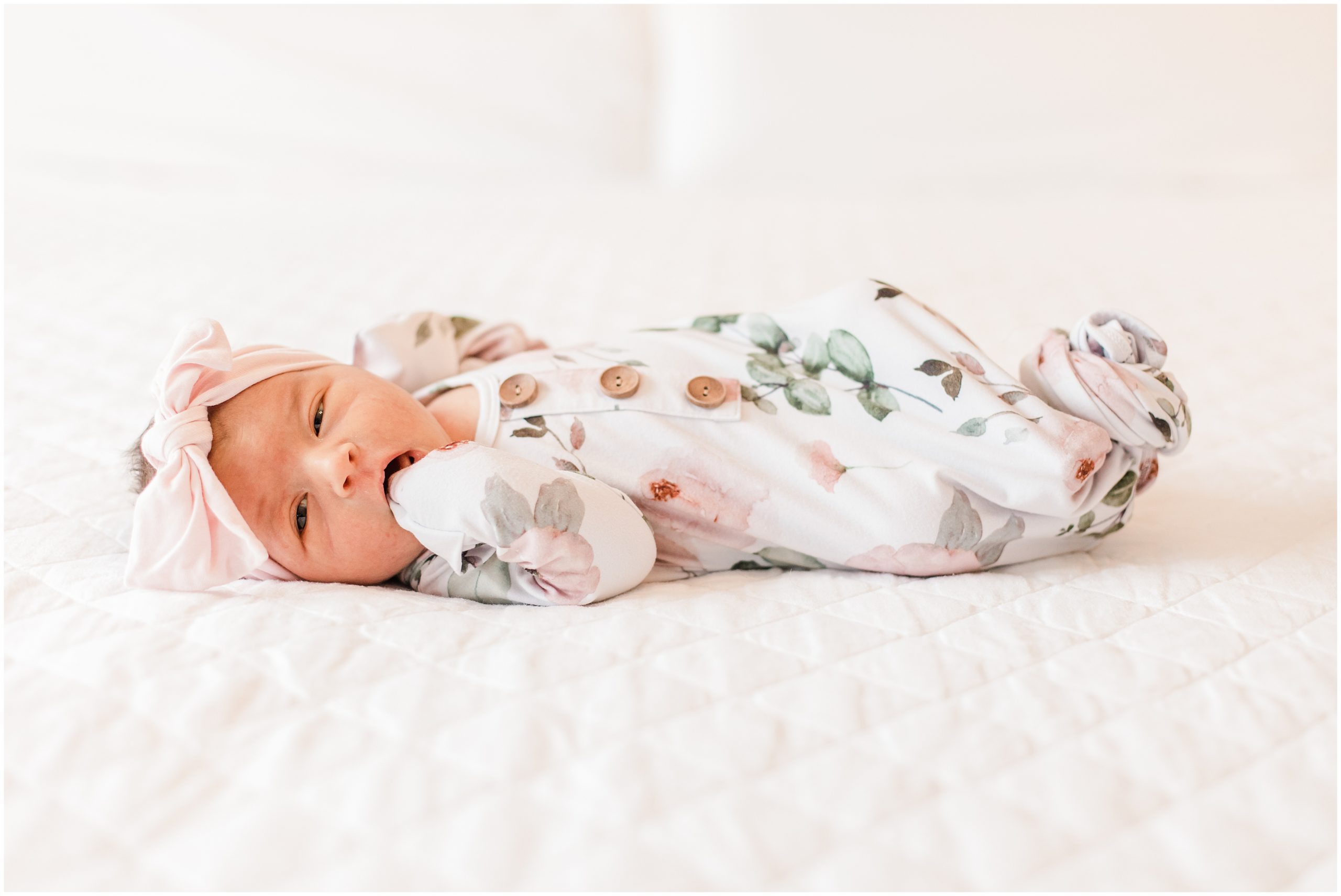 baby in floral onesie lays on bed during newborn photos at home 