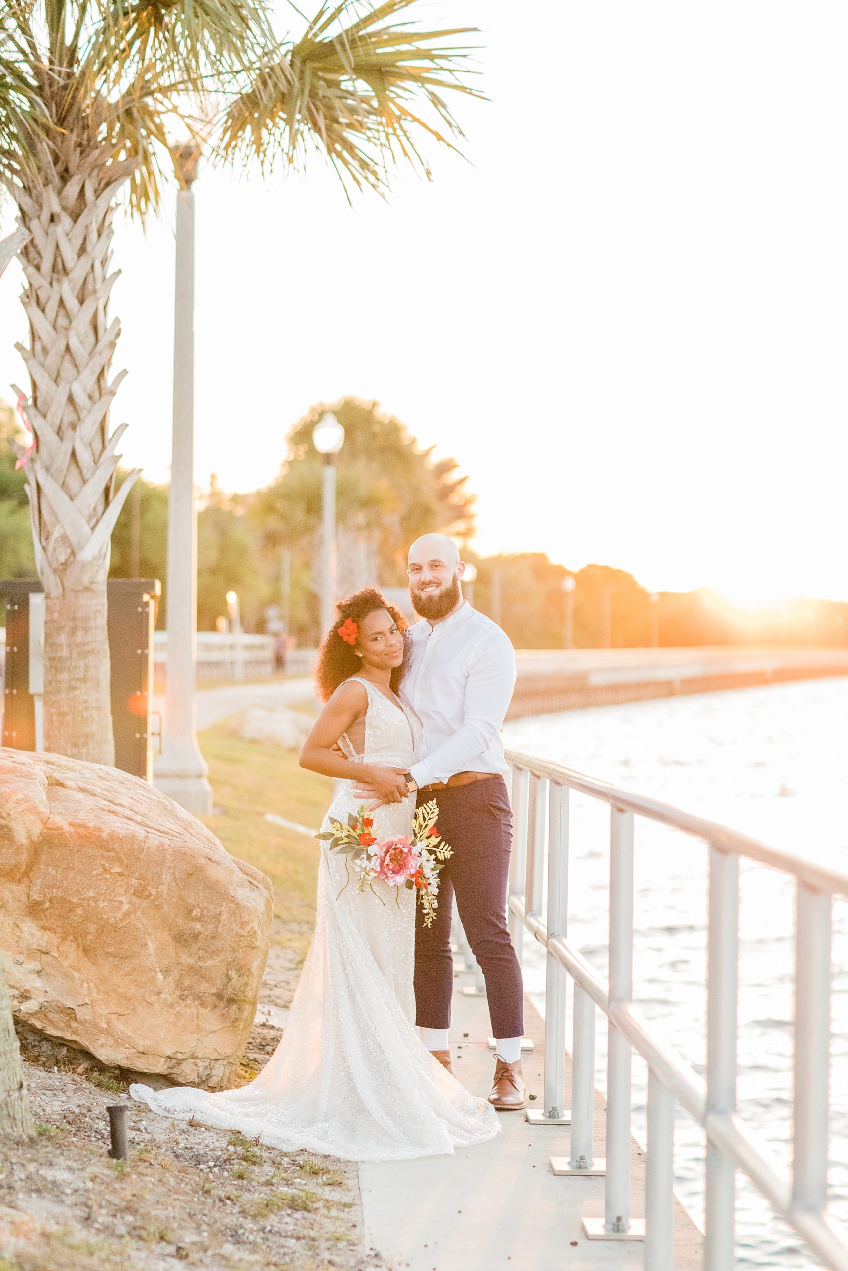 bride and groom hug at sunset along pier in Veteran's Park