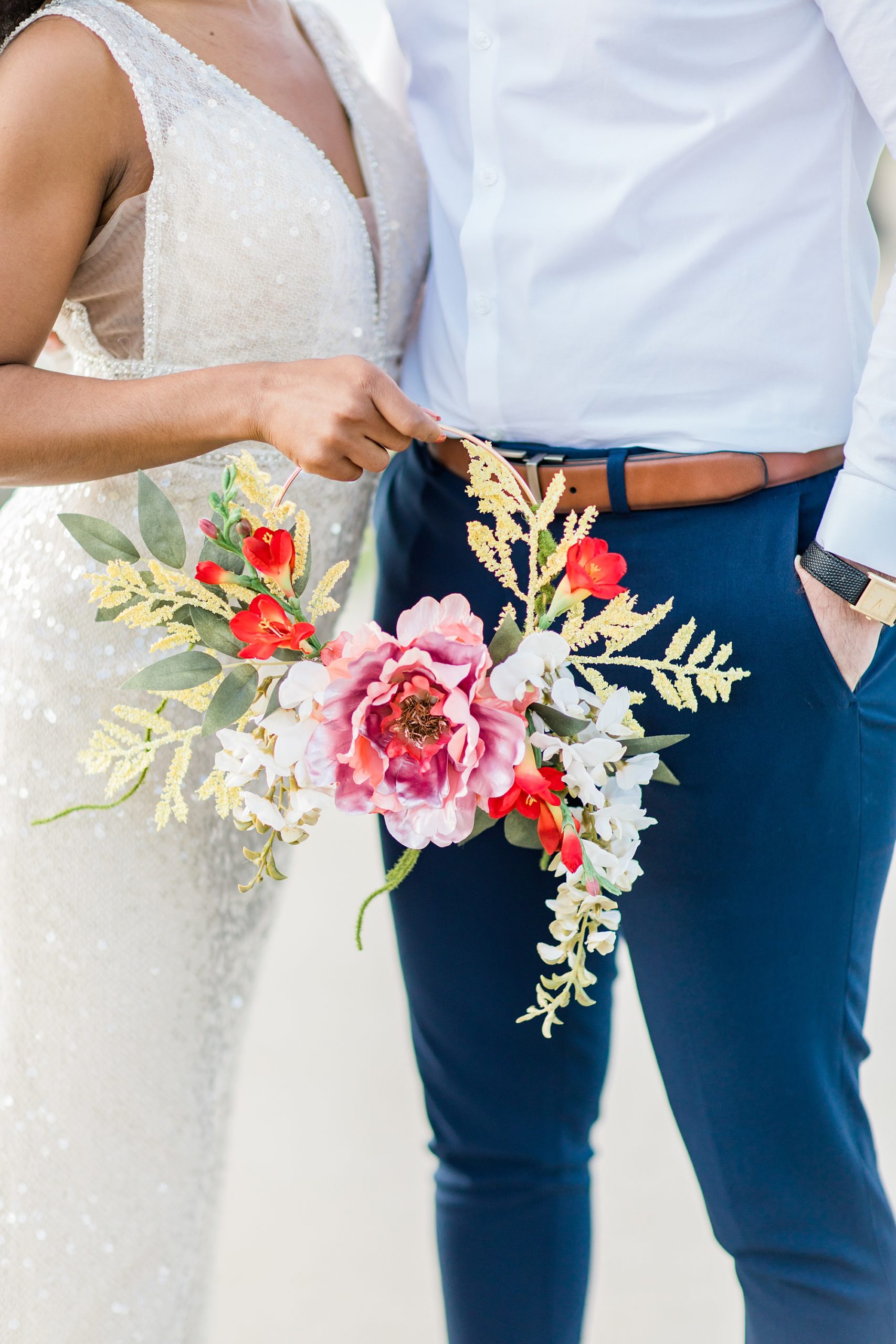 bride holds circular flower holder with bright tropical flowers