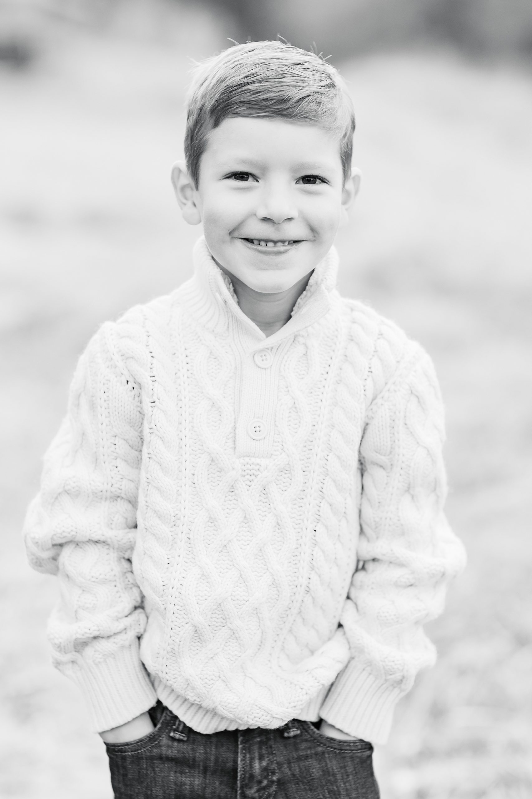 boy in cable knit sweater smiles with hands in his pockets during fall family photos