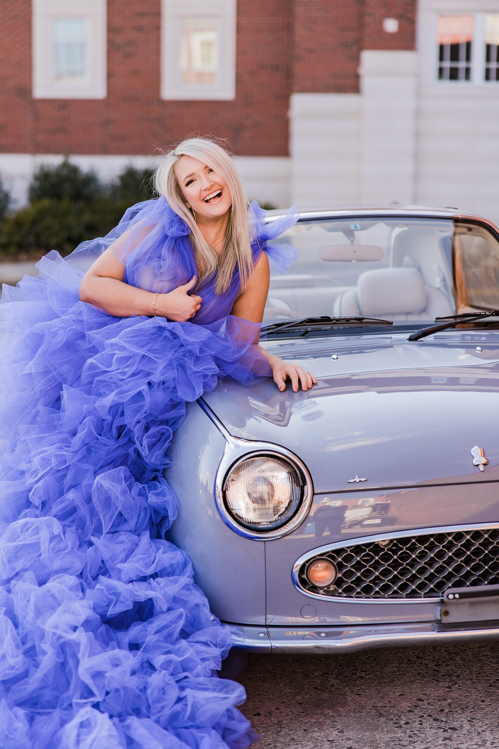 makeup artist in dramatic purple gown leans against car