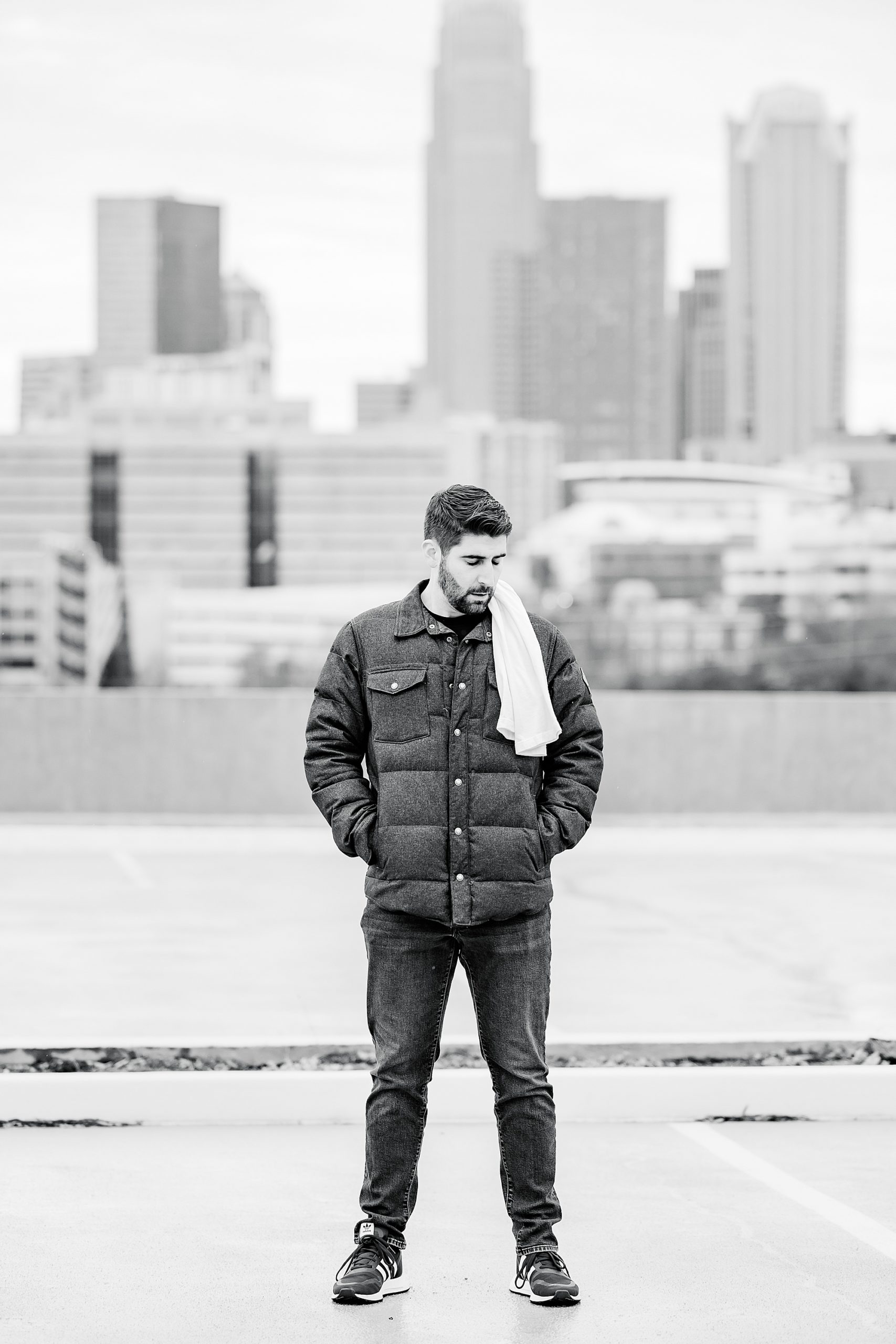 man stands in winter coat by Charlotte skyline 
