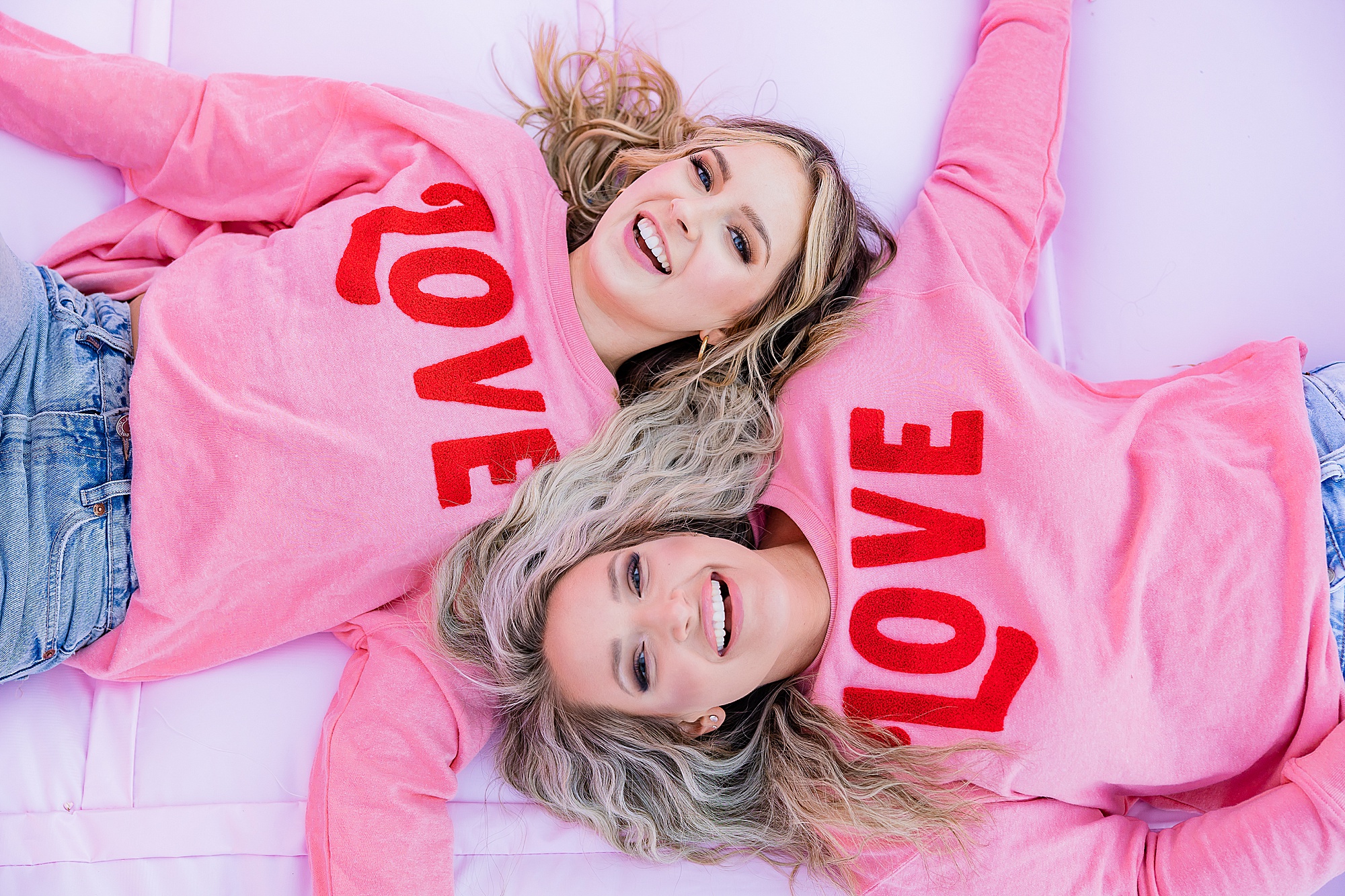 women lay on bounce house in matching LOVE Sweaters 