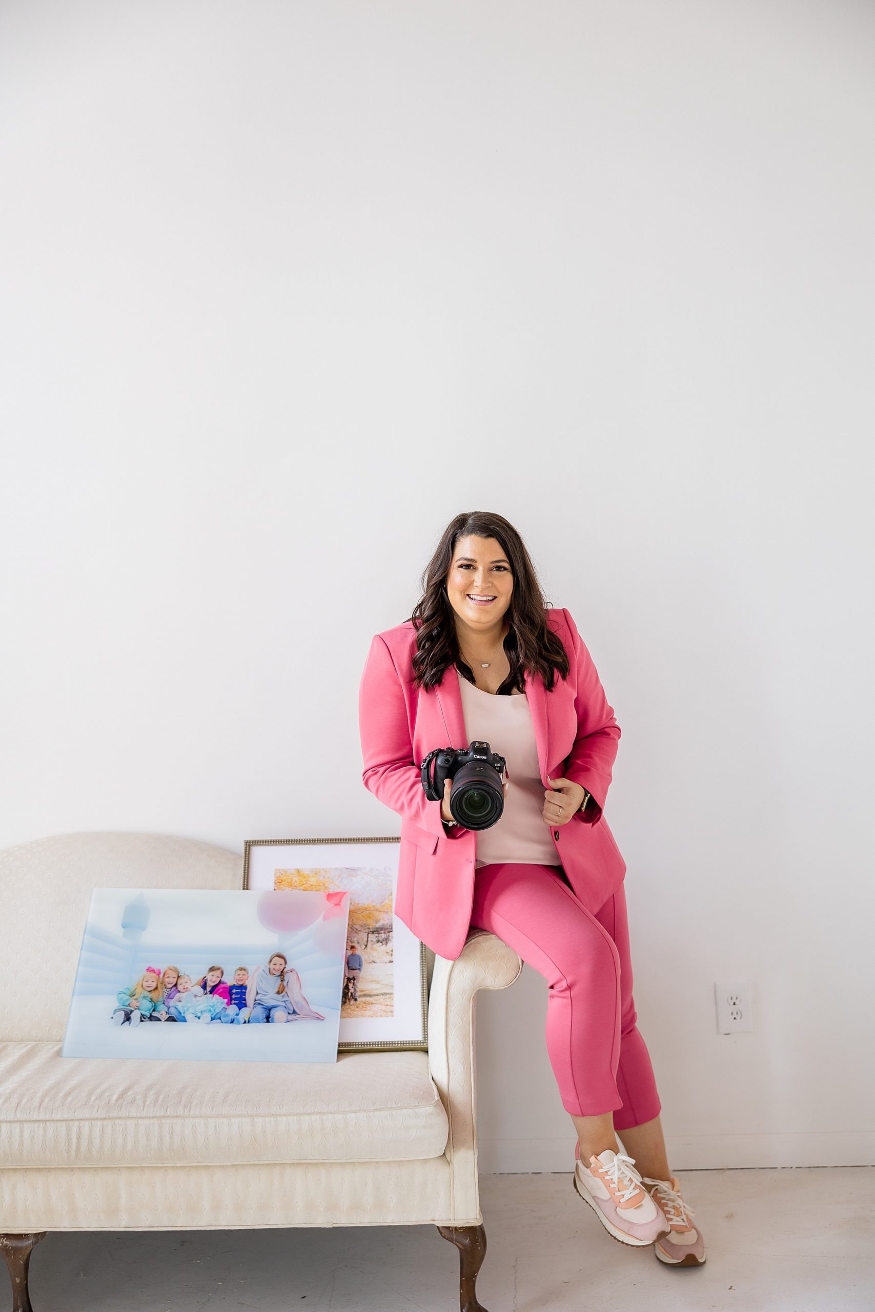 photographer in pink pantsuit holds camera and printed images in studio