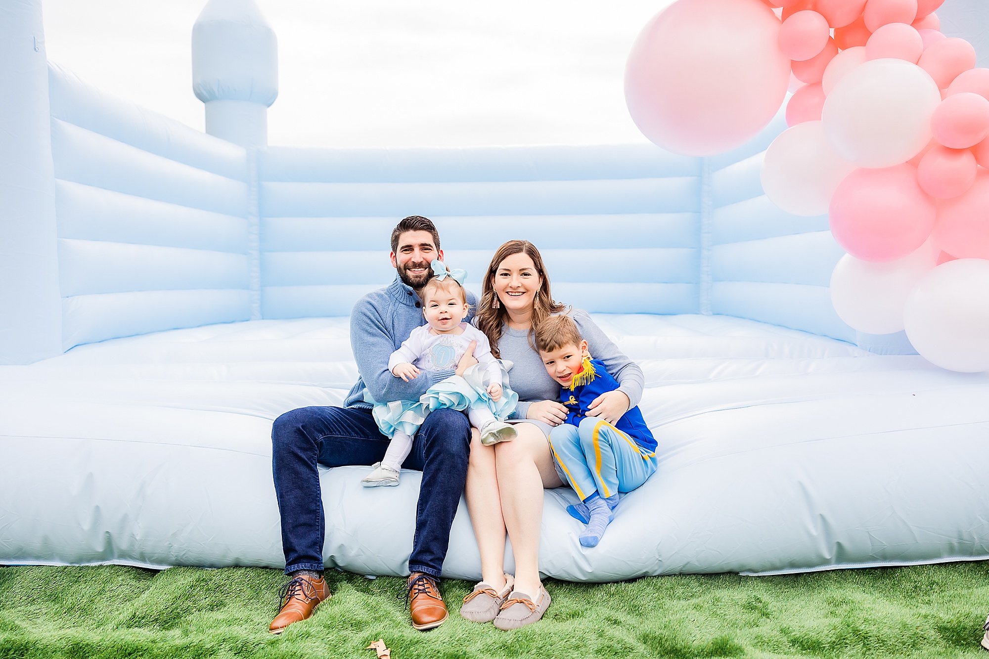 family of four sits n bounce house during Princess themed first birthday party