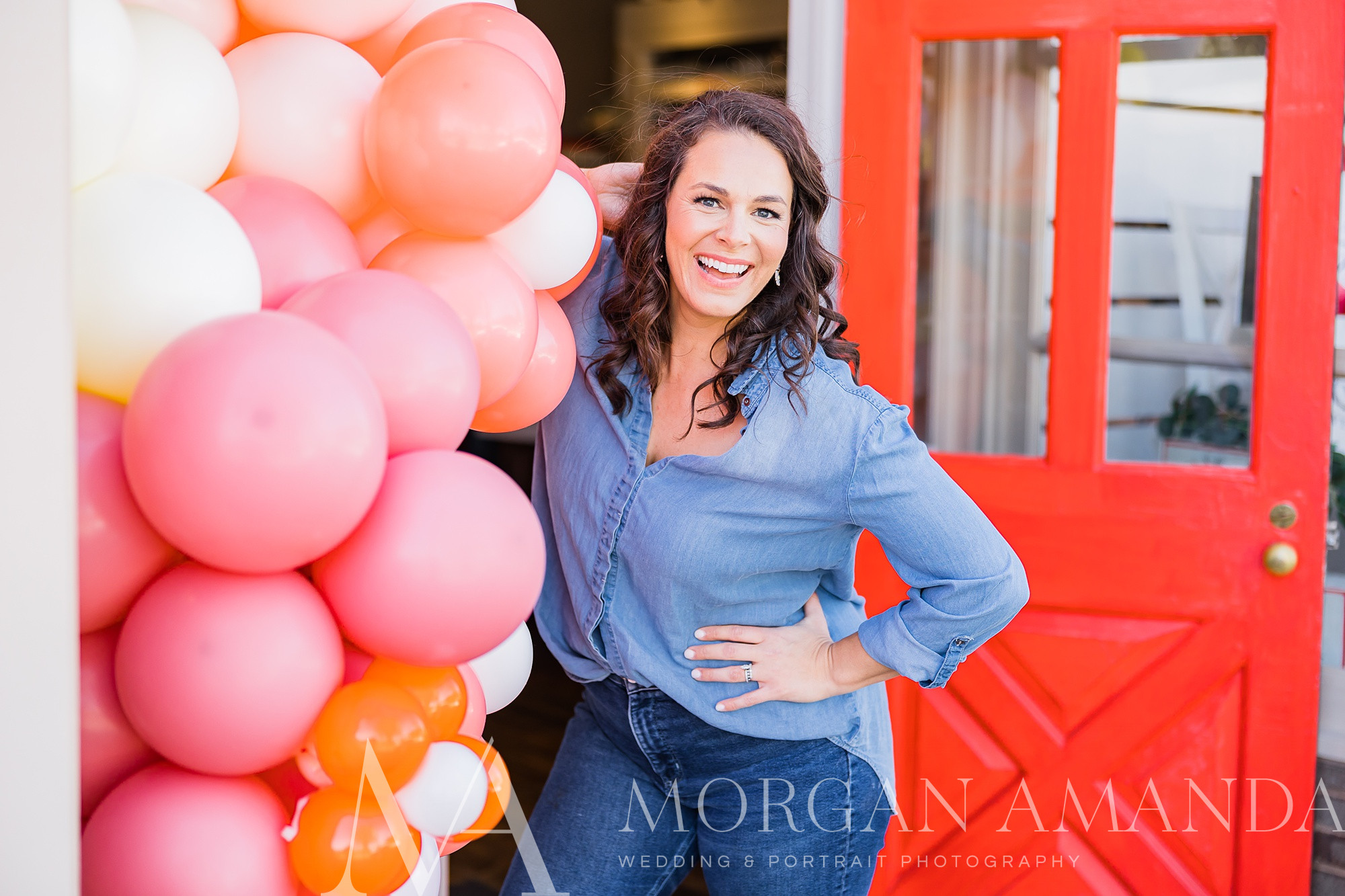 business owner leans against red door with balloon arch