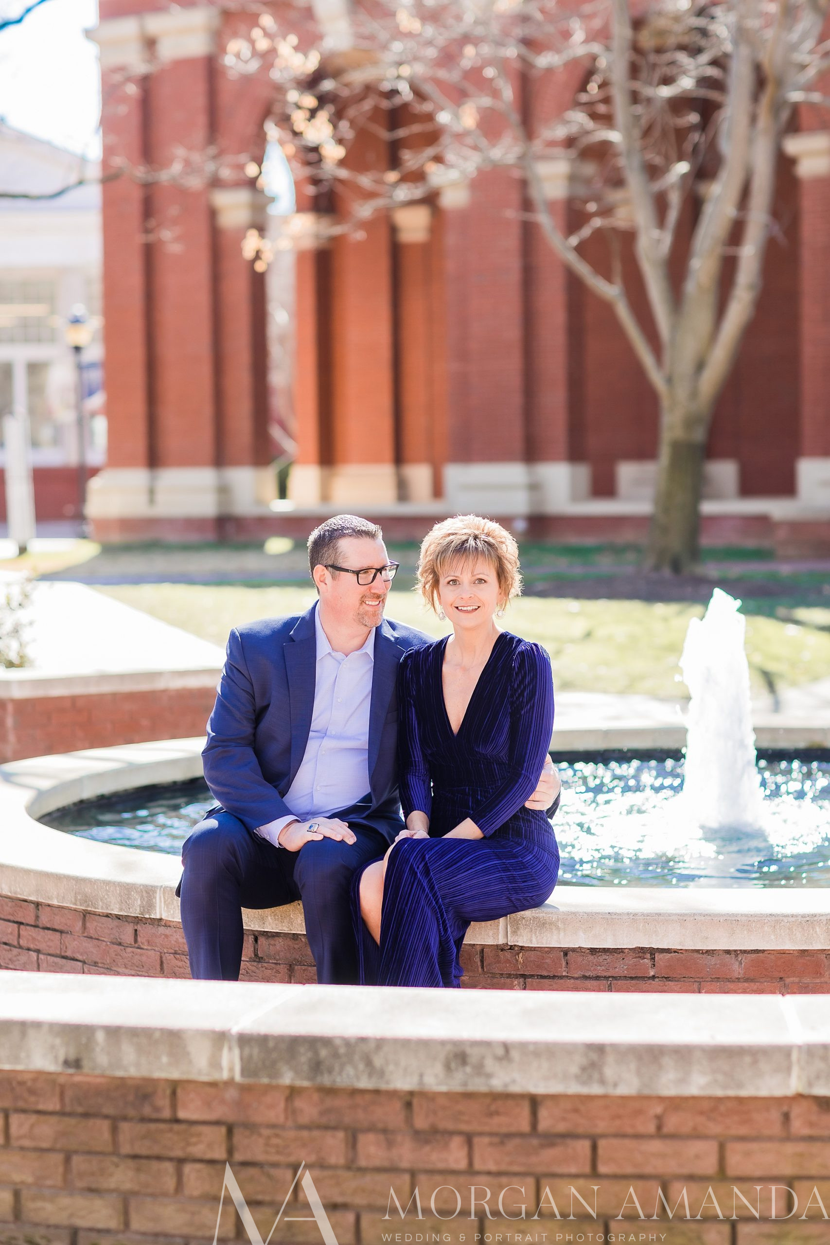 man and his fiancee sit on edge of fountain at Queens University
