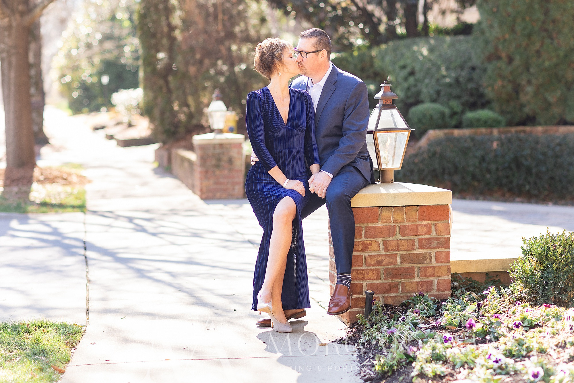 engaged couple sit on brick wall at Queens University