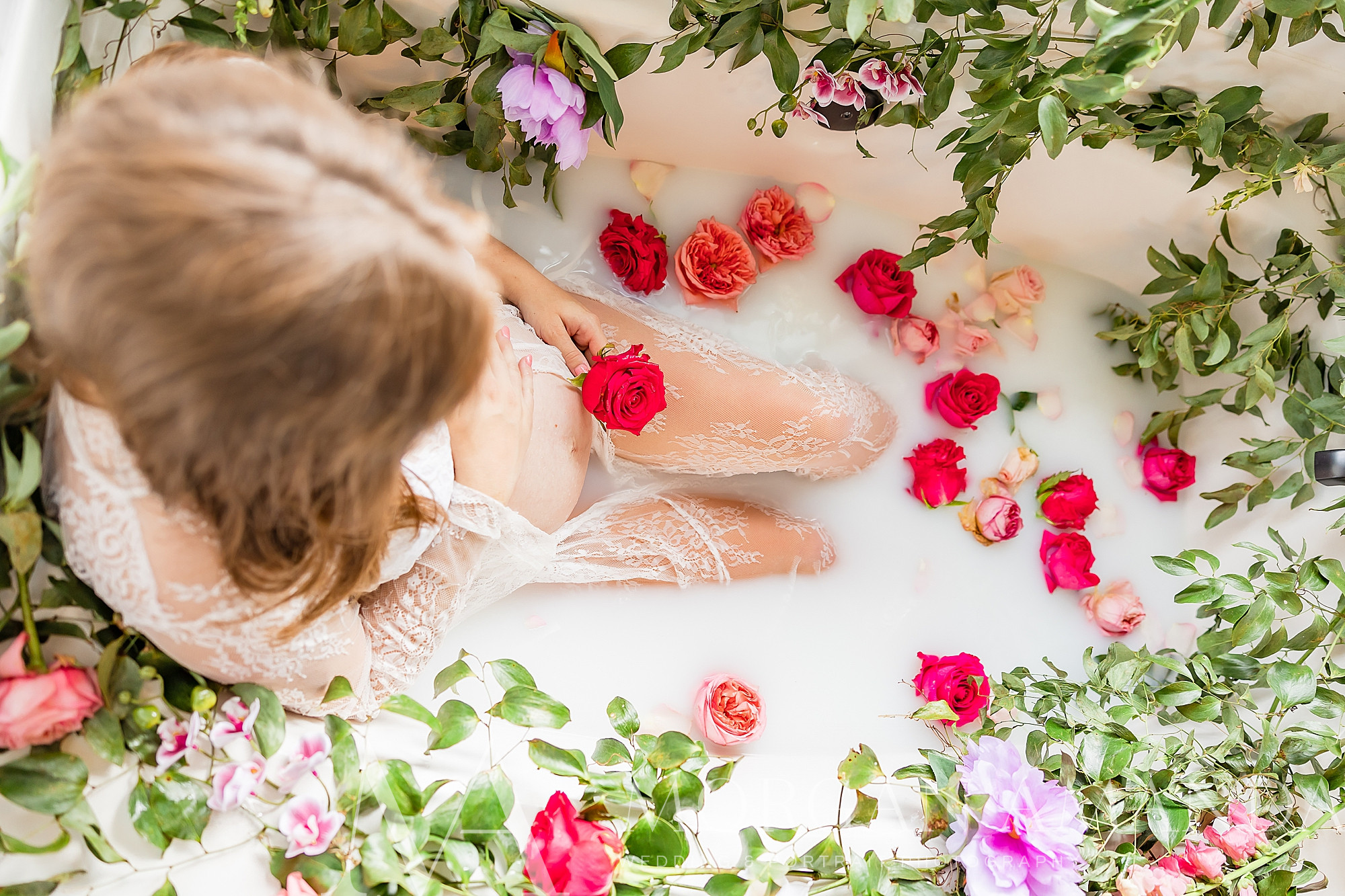 woman lays in tub with flowers and milk during maternity photos