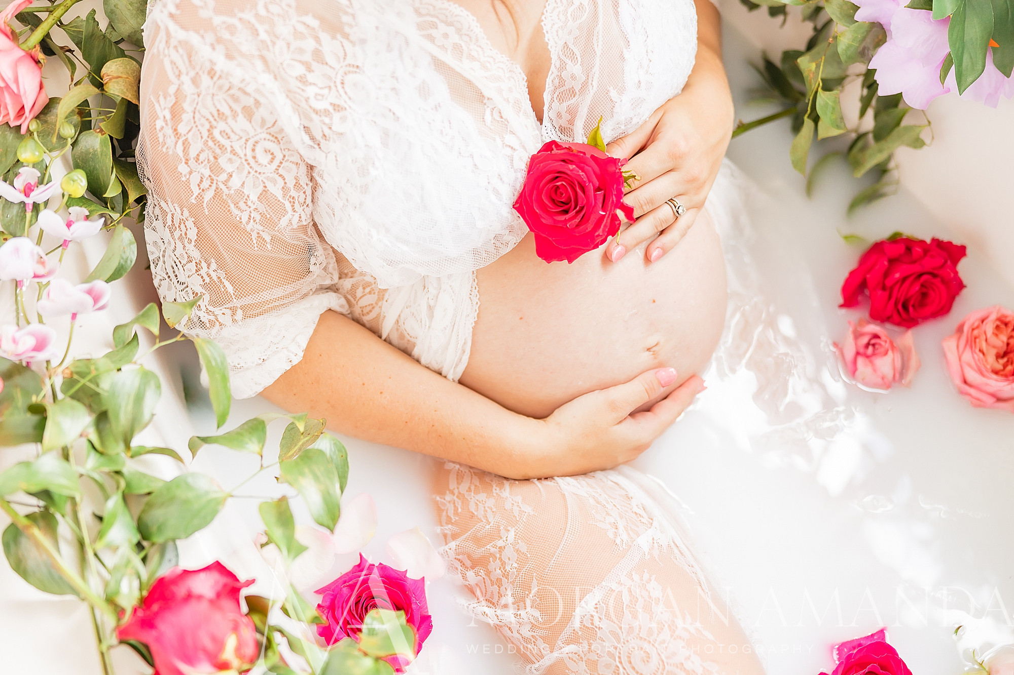 woman holds flower to belly wearing white dress during maternity photos in tub
