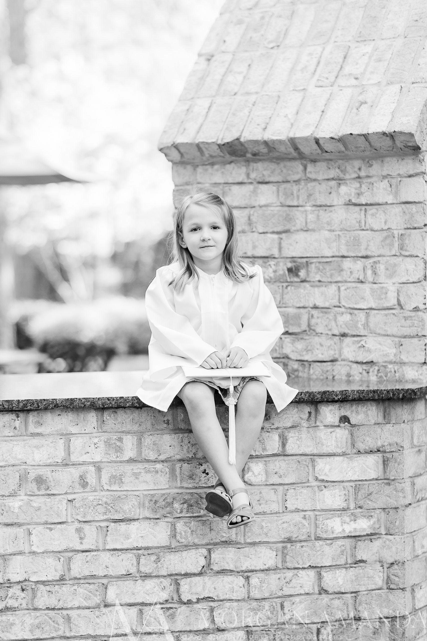 girl sits on brick wall in kindergarten graduation outfit