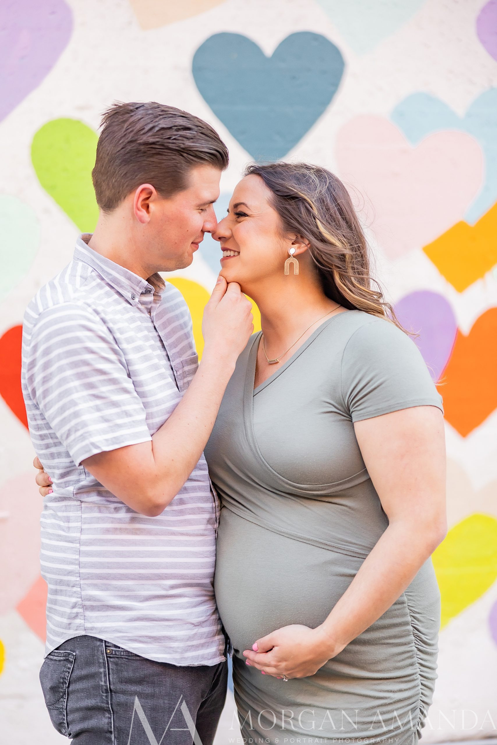 man holds woman's chin making her laugh during Uptown Charlotte maternity photos
