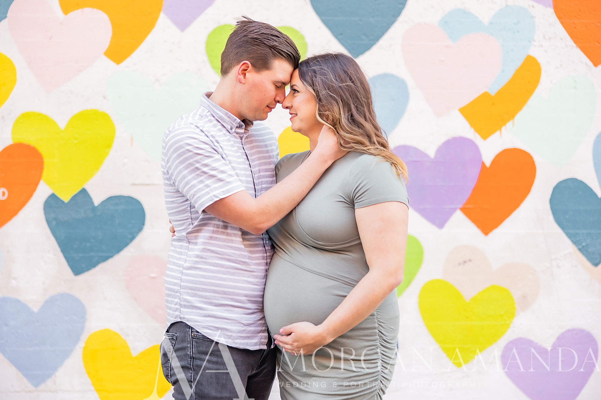 woman holds her belly bump while her husband leans into her