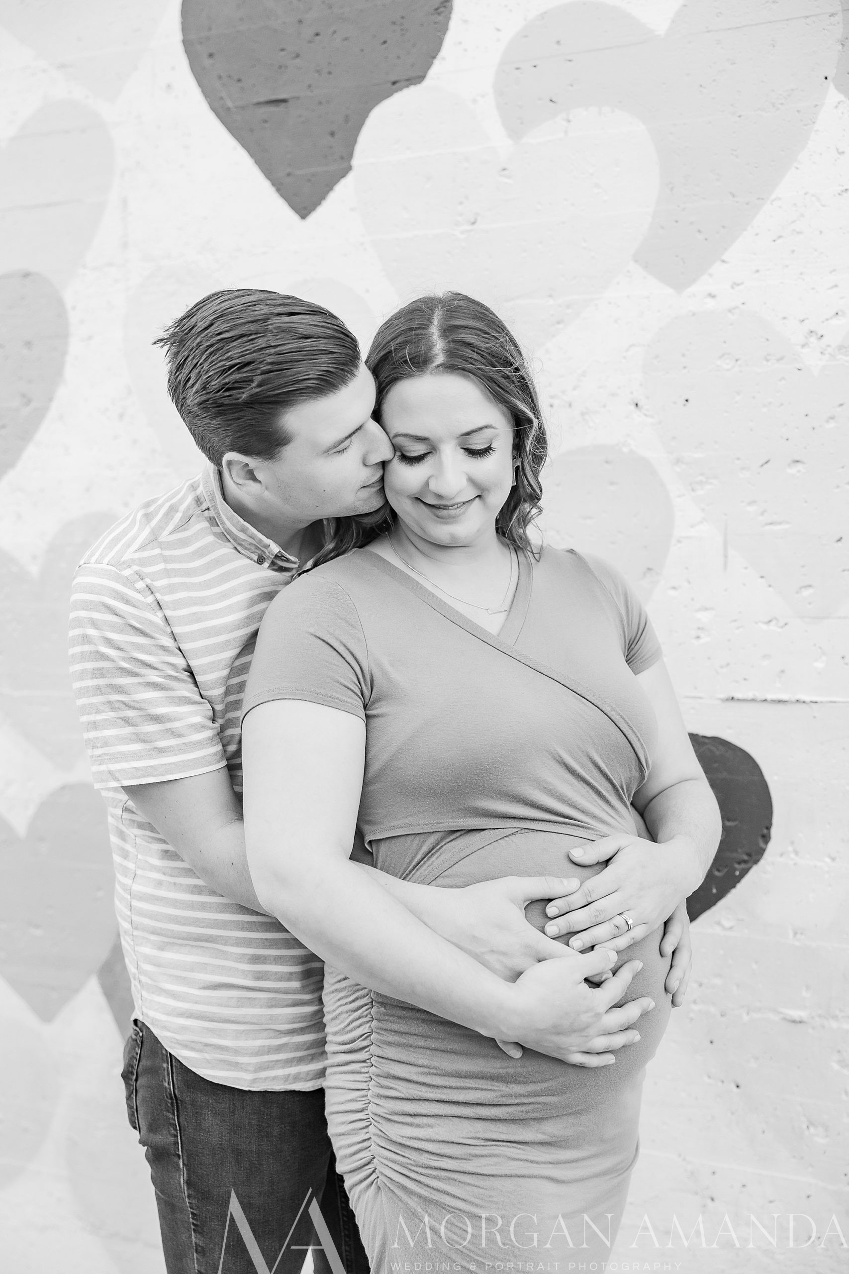 man hugs wife around belly during maternity session against wall in Uptown Charlotte 