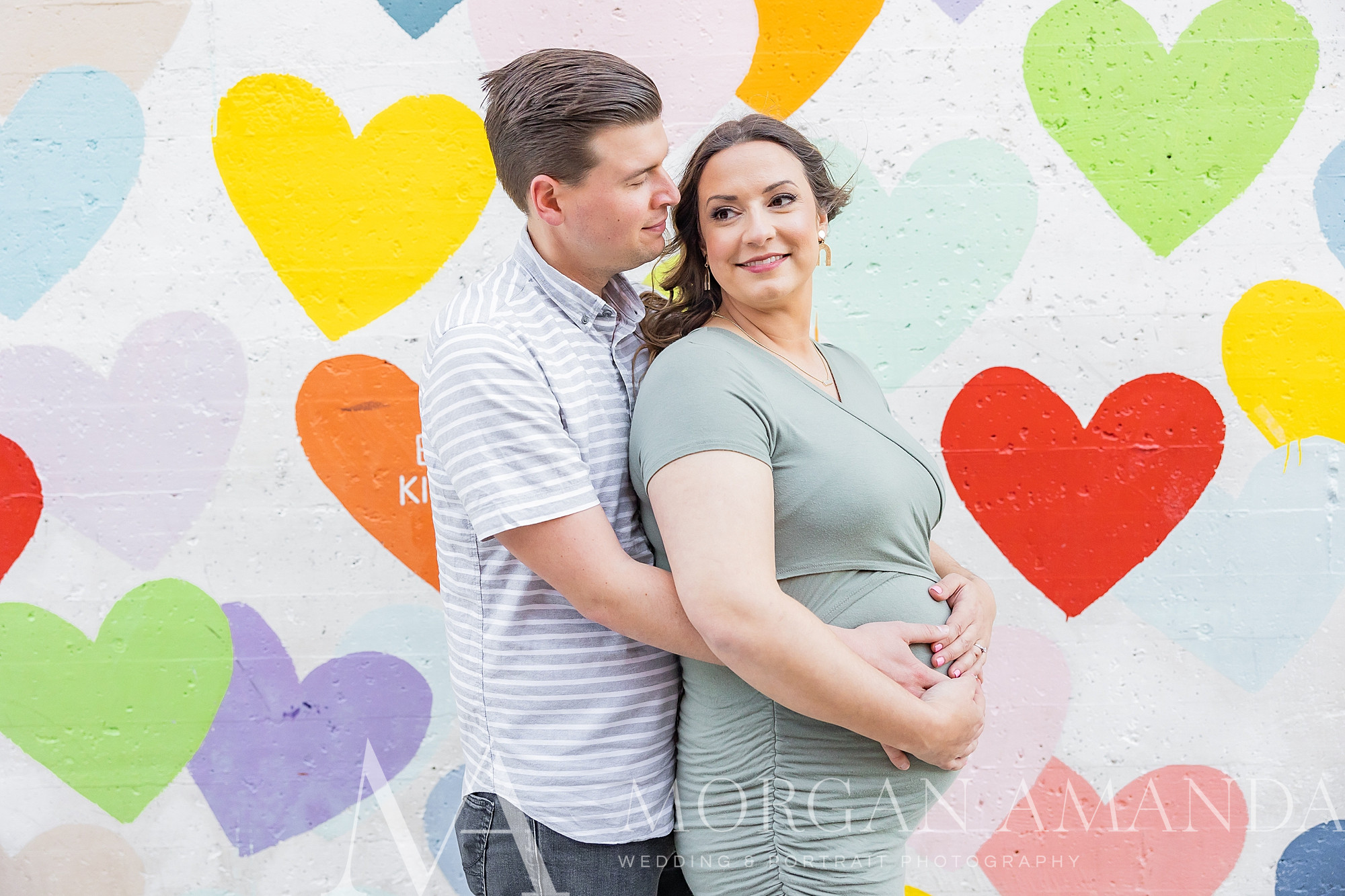 man hugs wife from behind holding baby bump during maternity photos in Uptown Charlotte 