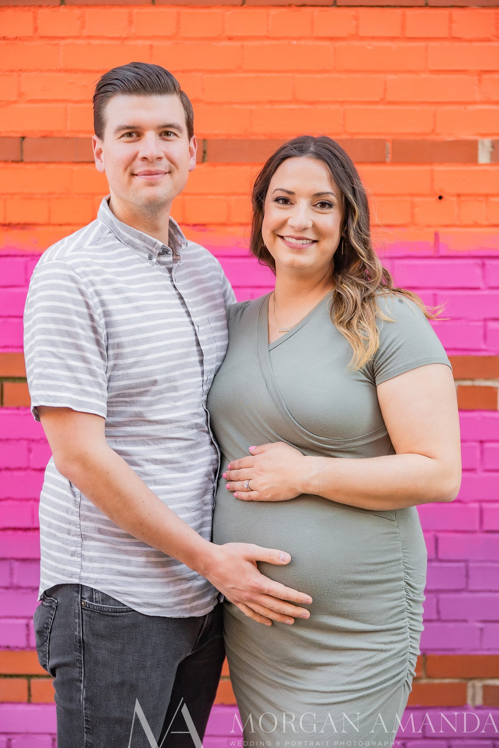 couple stands by colorful wall holding mom's baby bump