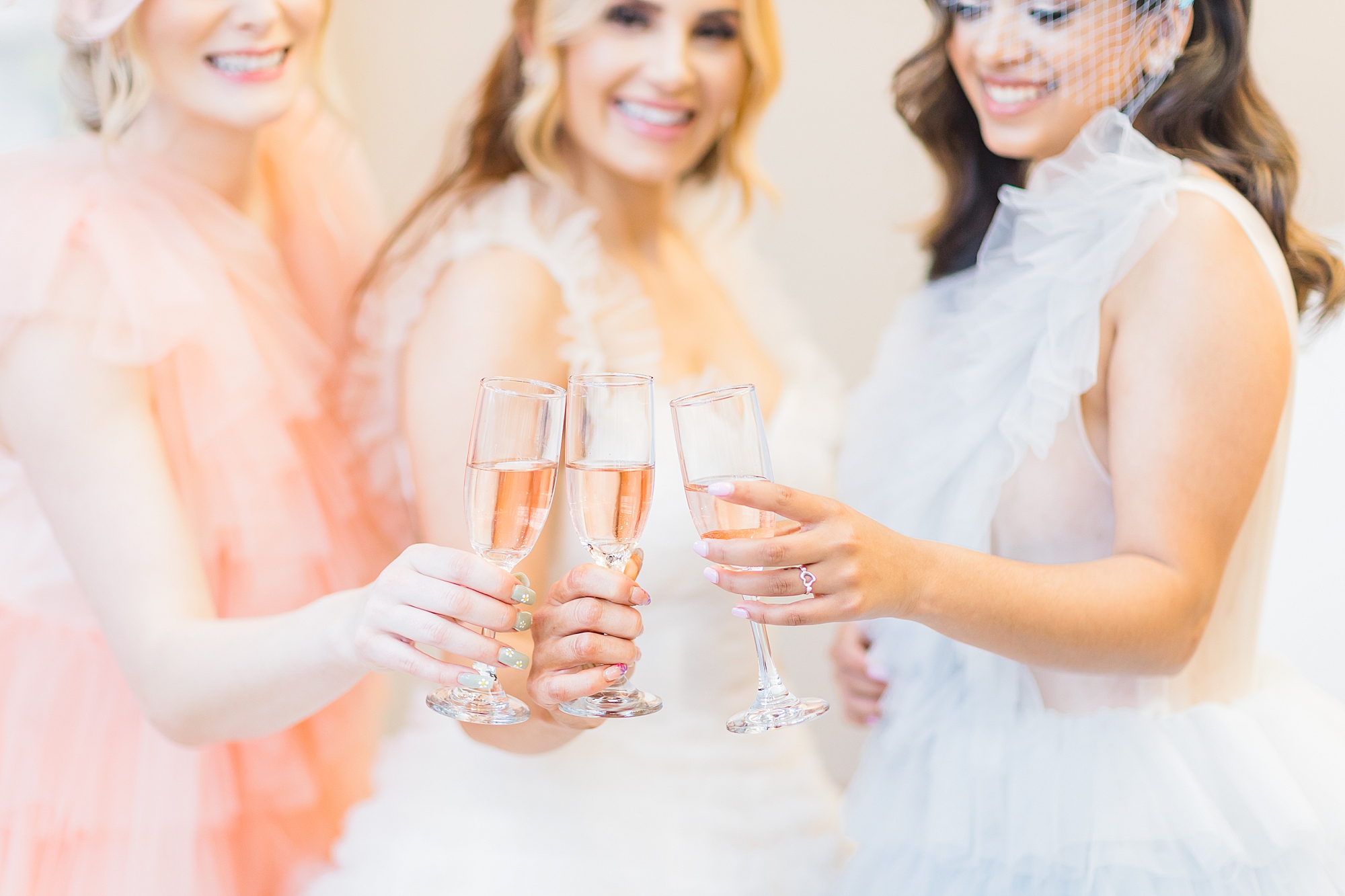 three women in pastel gowns toast champagne