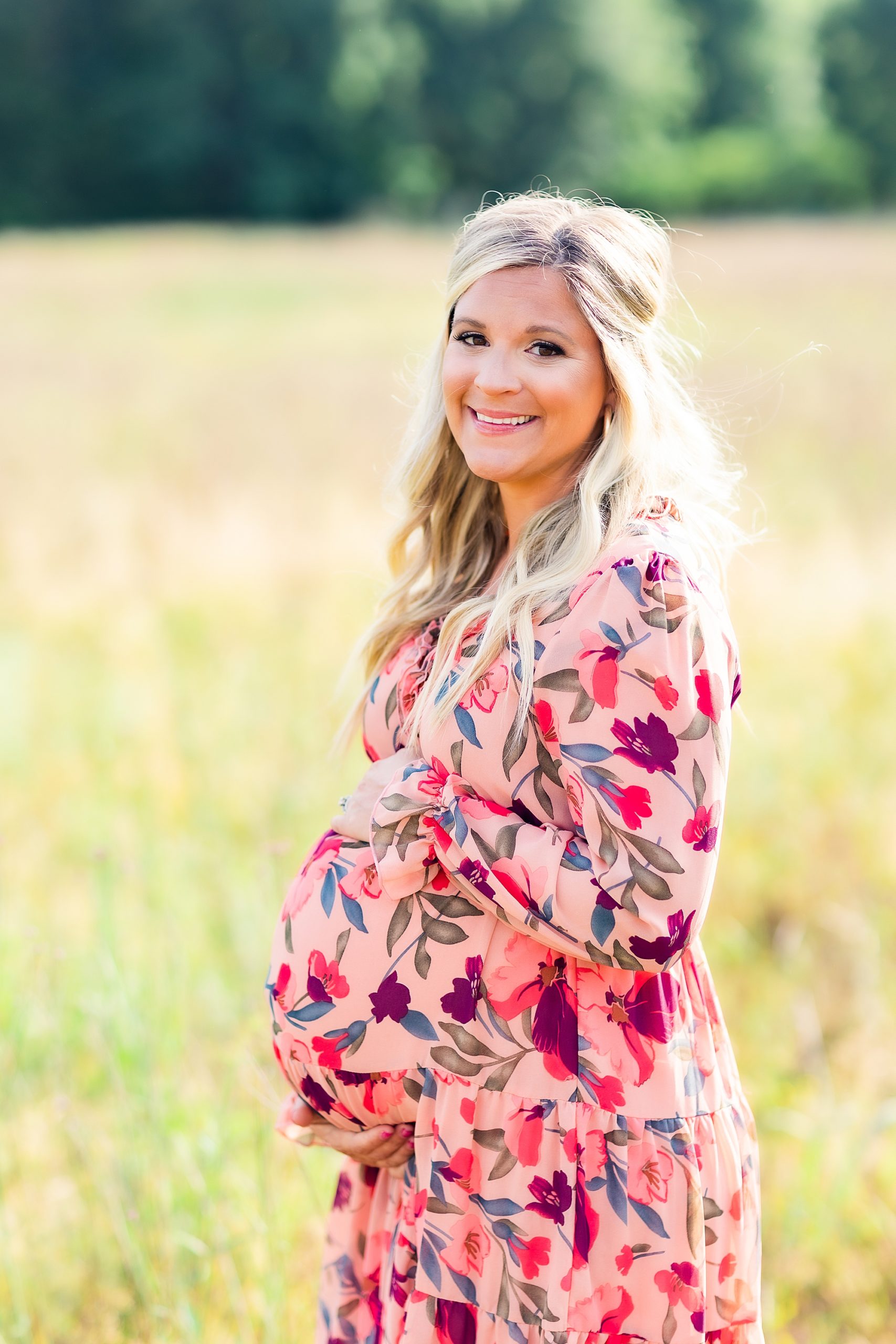 expecting mom holds baby bump wearing floral pink gown