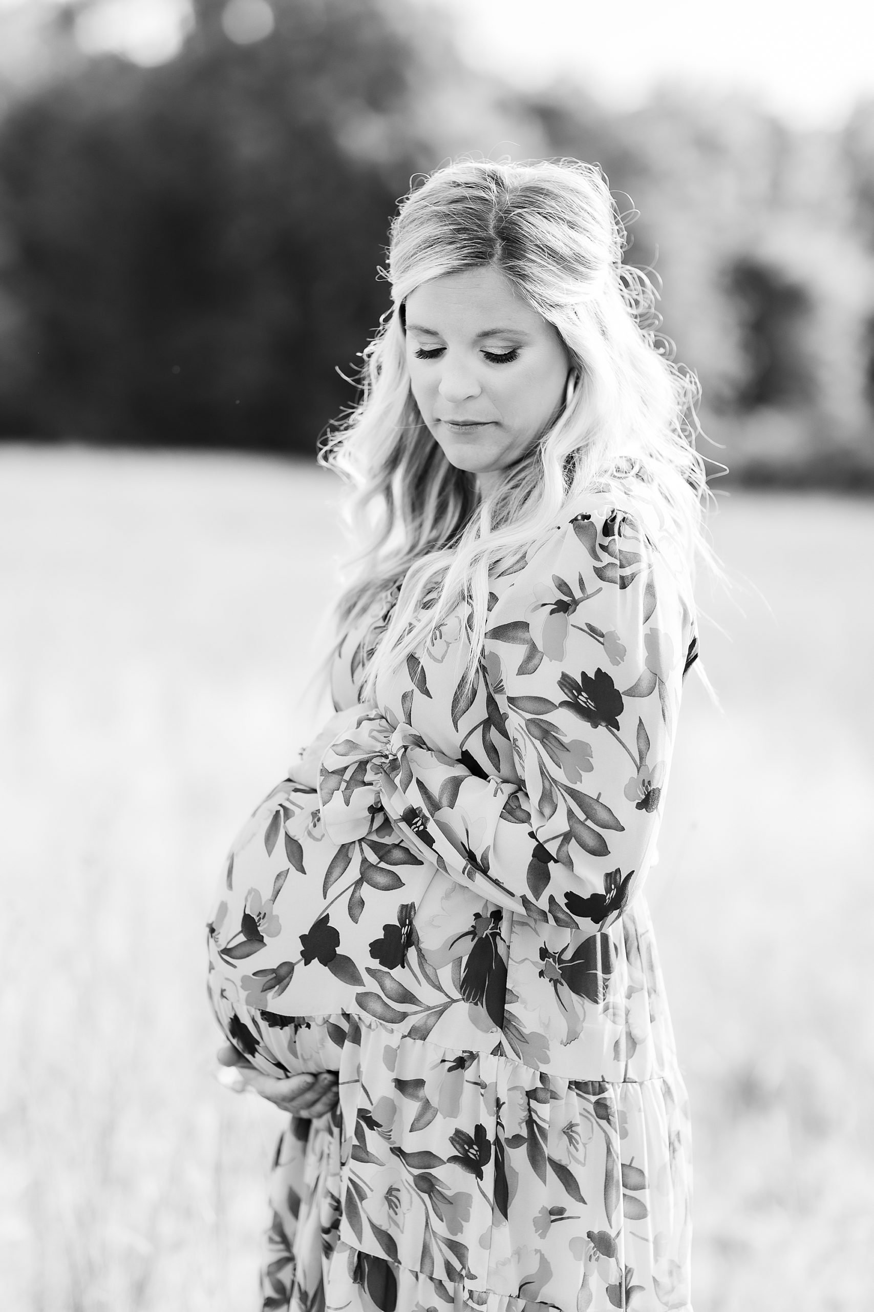 expecting mother stands in Charlotte field wearing floral gown