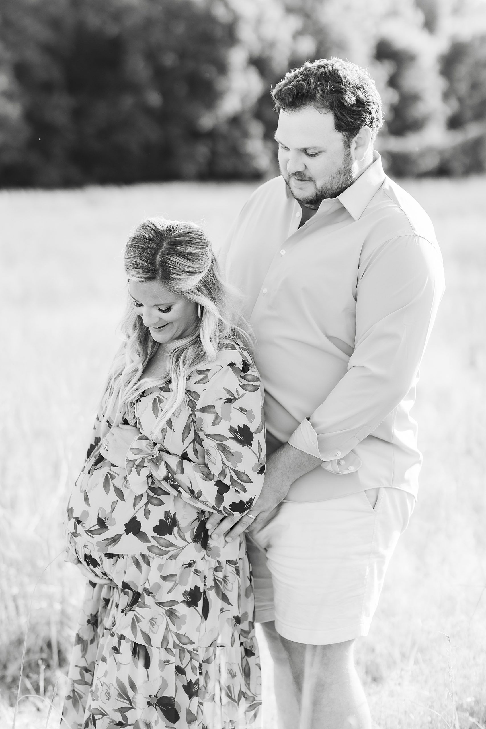 expecting parents stand together during maternity portraits in Charlotte field