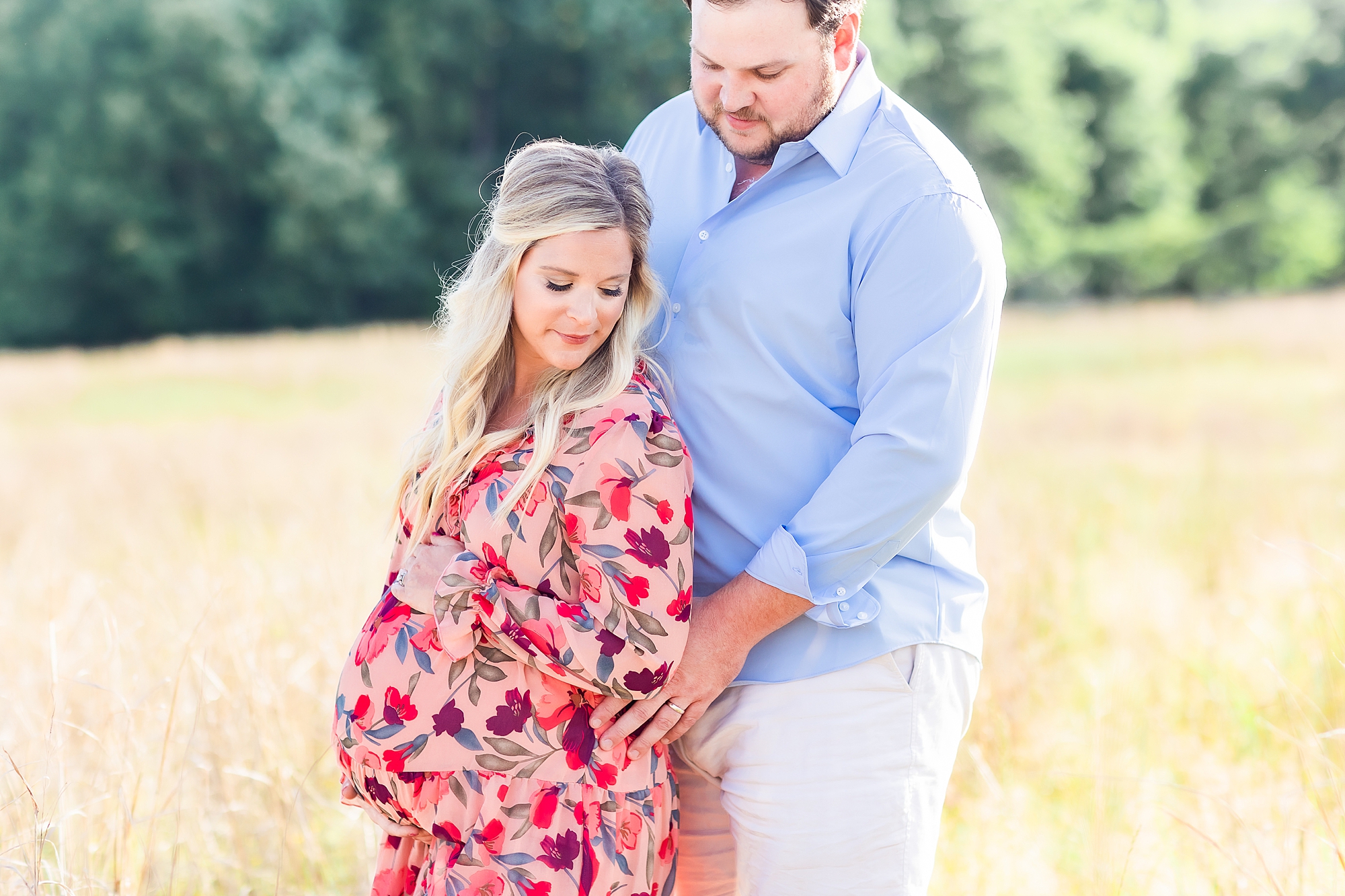 expecting parents hold mom's bump during photos in field