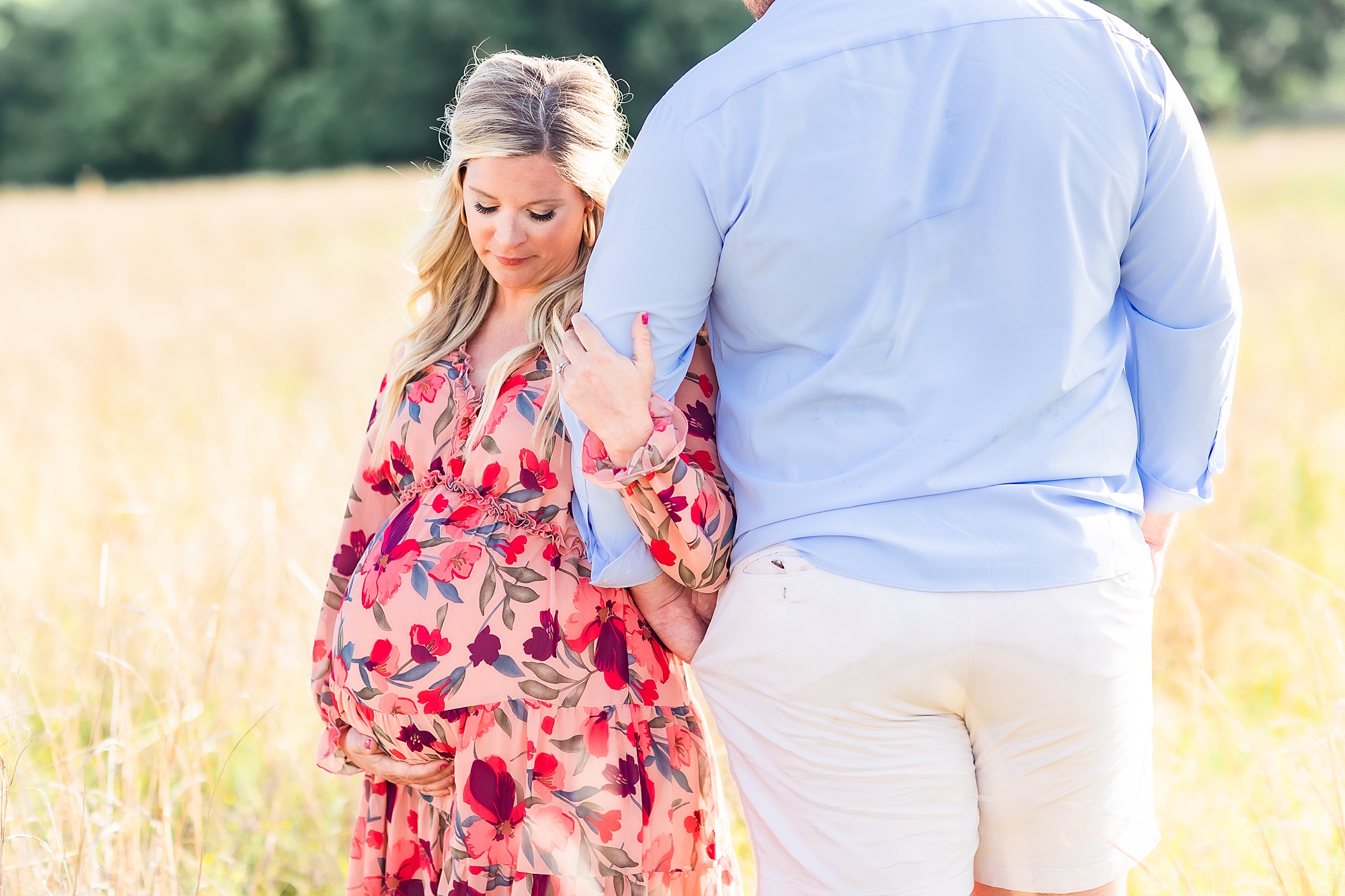 mom leans against husband's arm during maternity portraits in Charlotte field