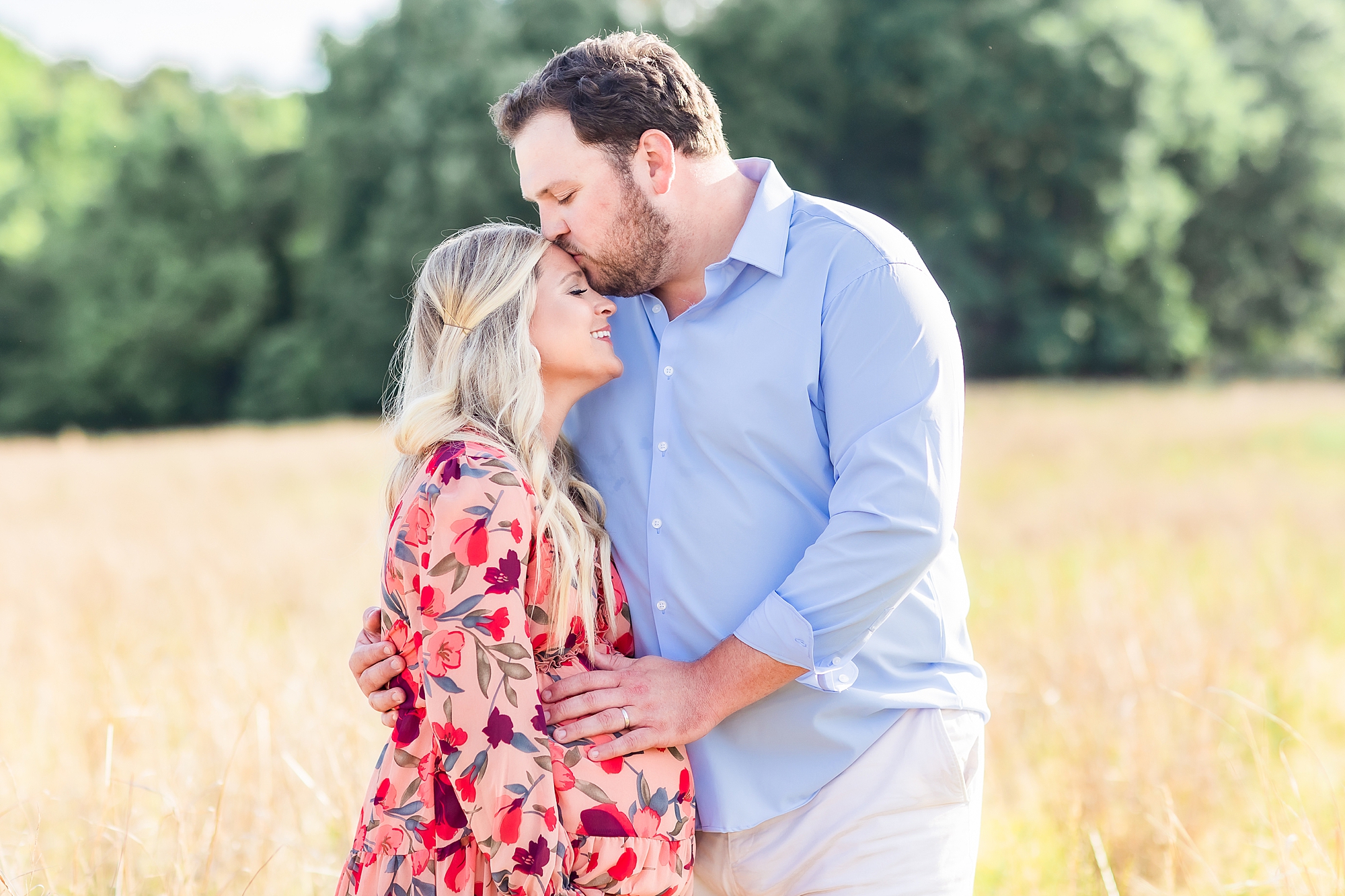 husband kisses wife's forehead during maternity portraits in Charlotte field