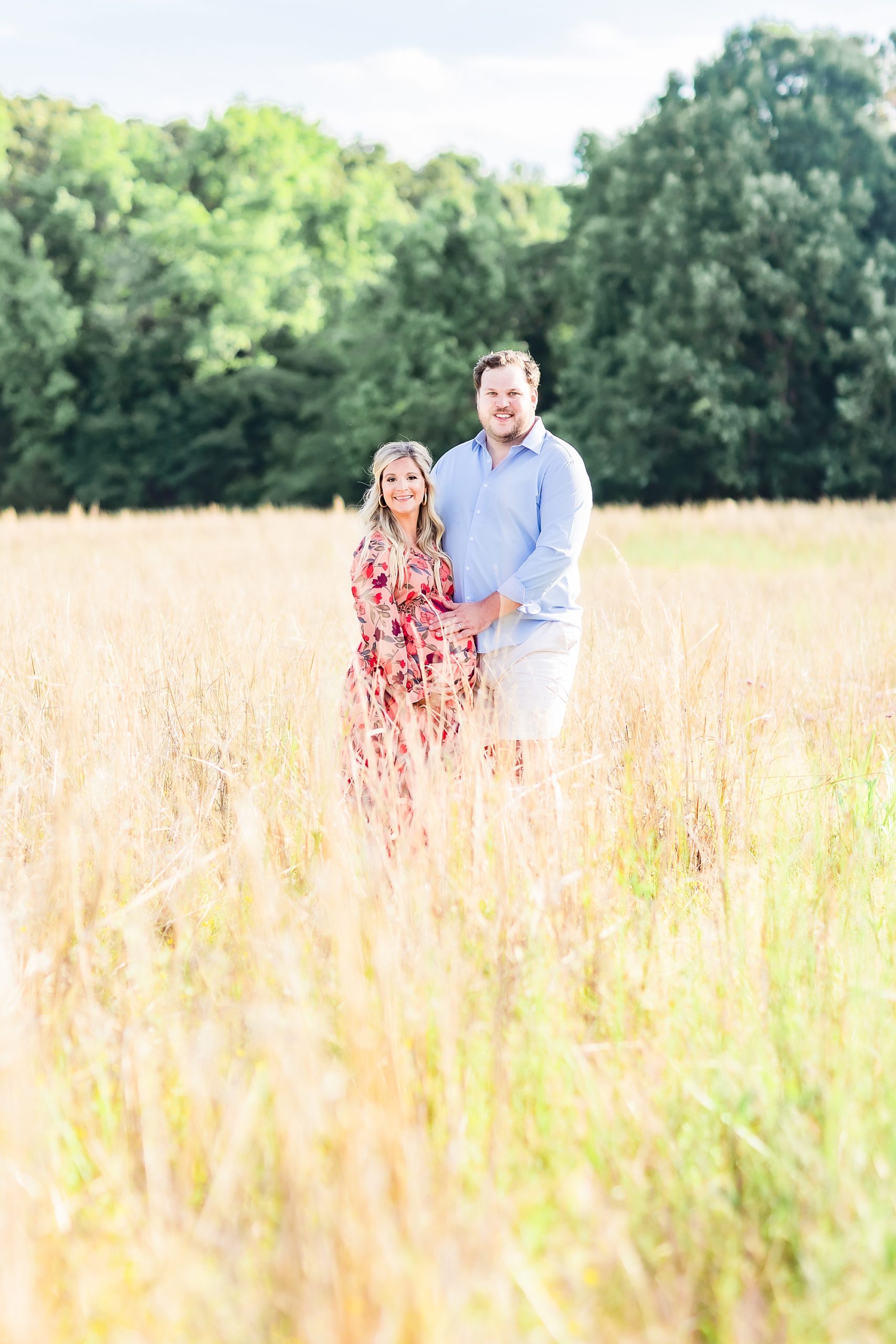 new parents stand holding woman's belly during maternity portraits in Charlotte field