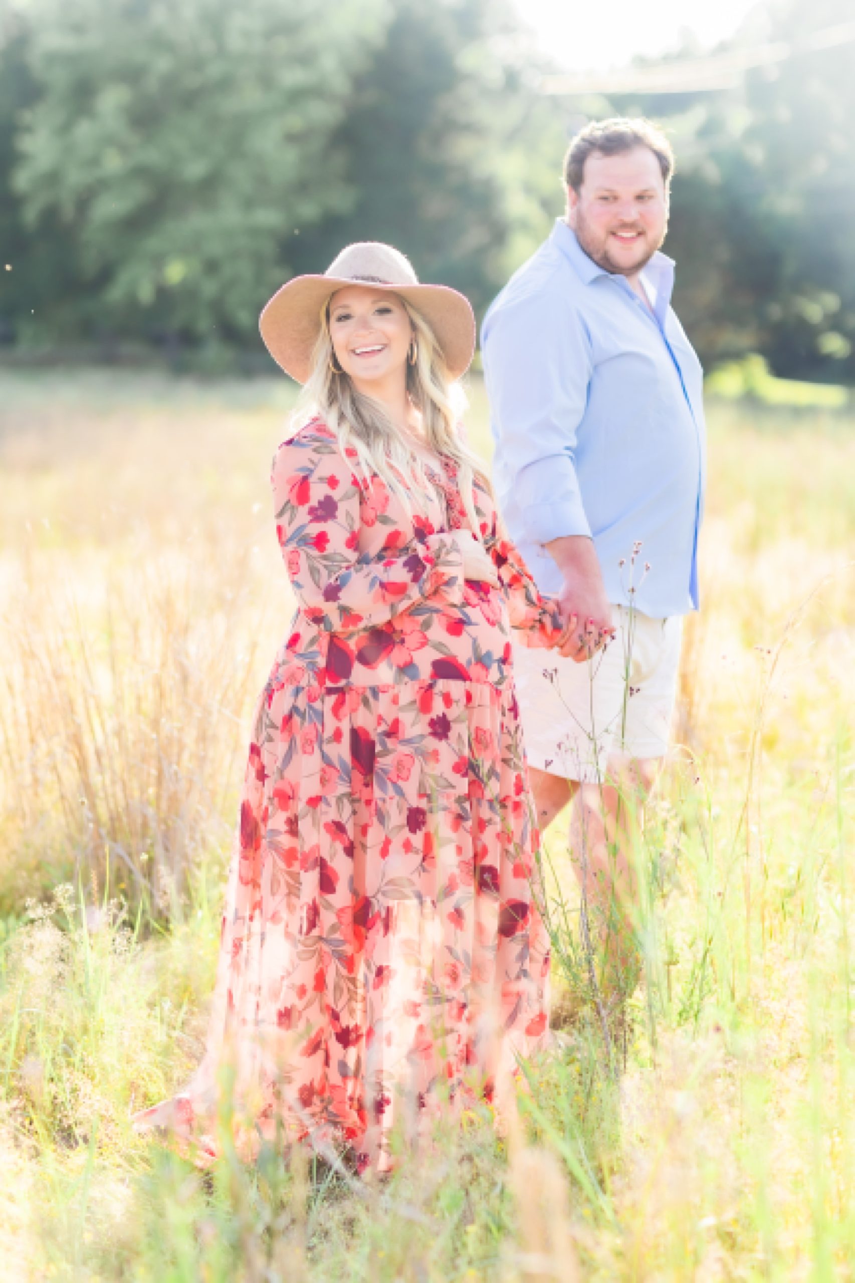 couple walks through field during maternity photos in field