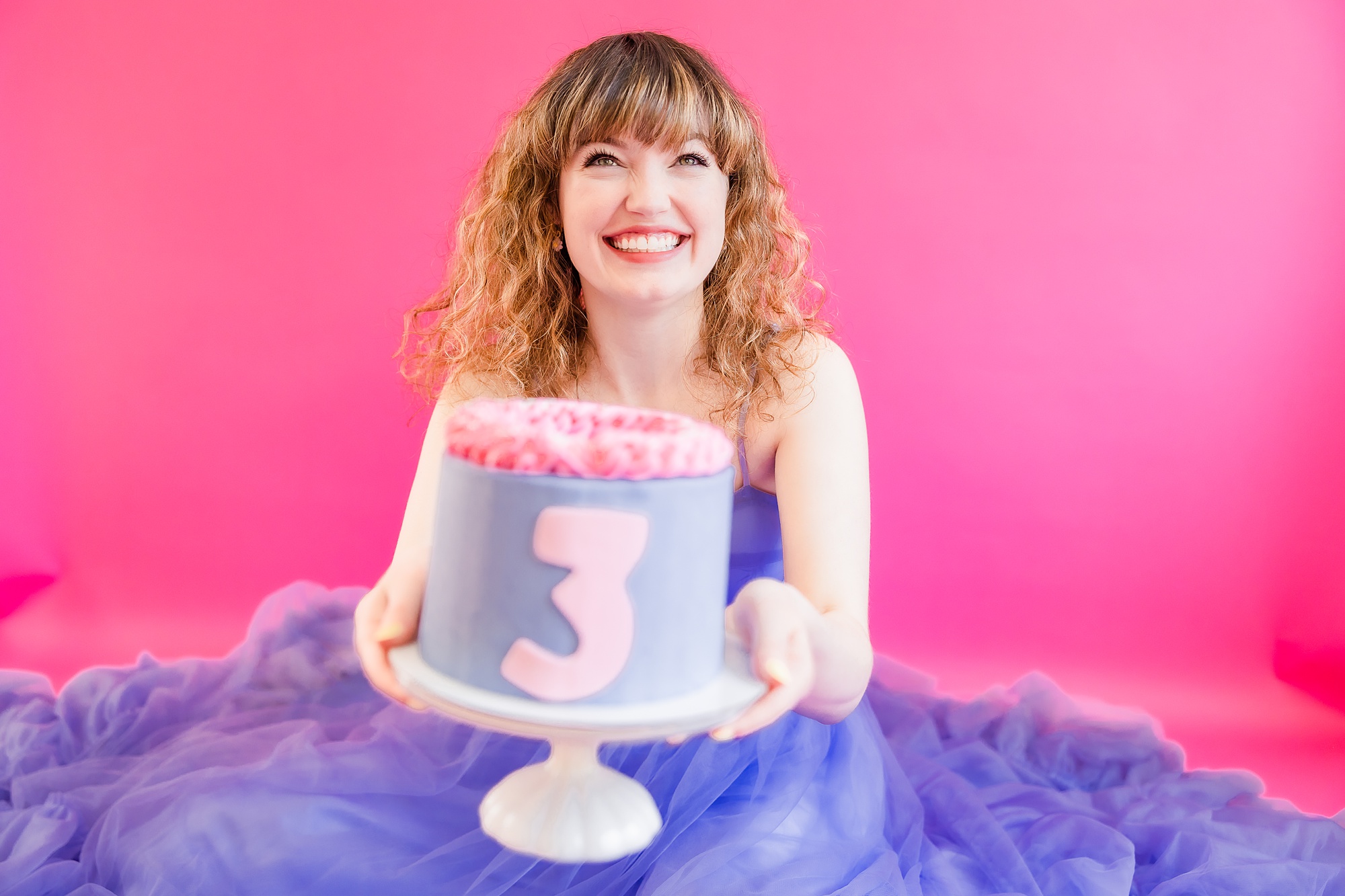 woman holds out cake with 3 on it for playful branding portraits