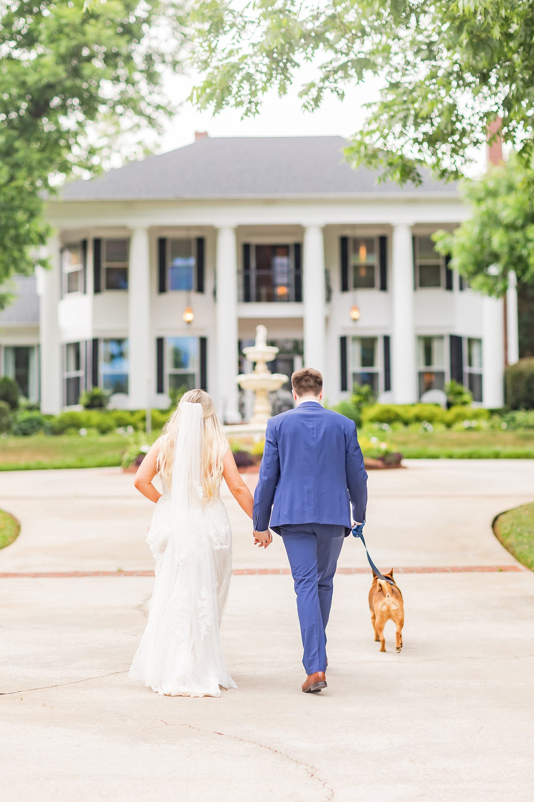 bride and groom walk with dog outside the Victoria Belle Mansion