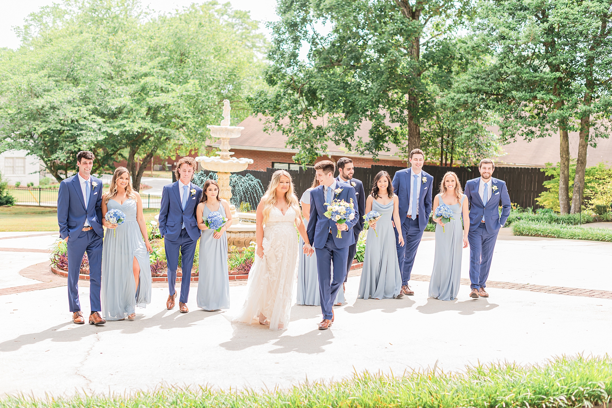 bride and groom walk with bridal party in light blue gowns and navy suits 